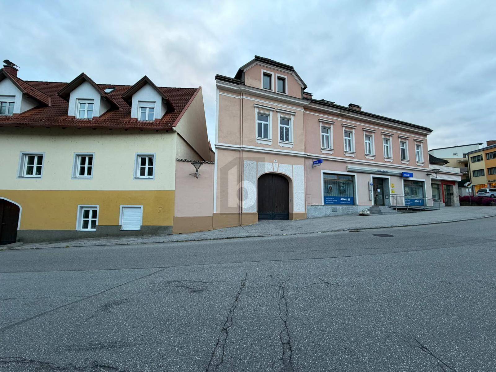 Historisches Gebäude mit Geschäften im Erdgeschoss und Wohnungen darüber an einer Straße.