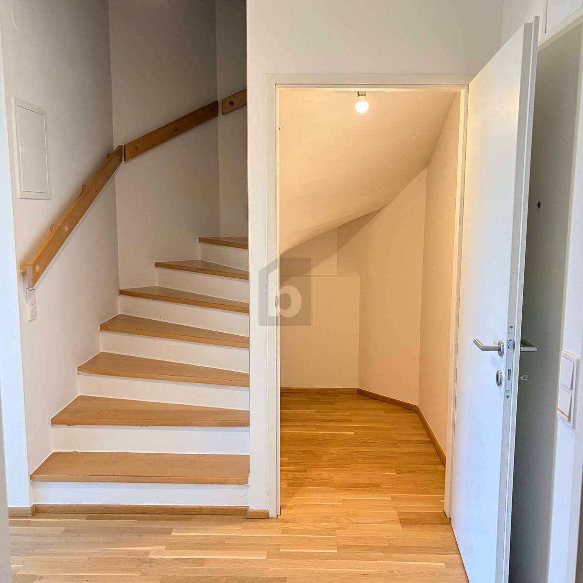 Heller Flur mit Holztreppe und Zugang zu einem kleinen Abstellraum unter der Treppe.