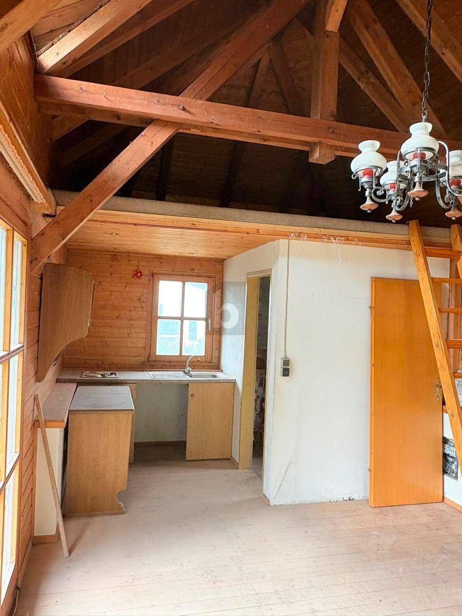 Rustikale Küchenzeile mit Spüle und einfachen Holzschränken unter freiliegenden Dachbalken.