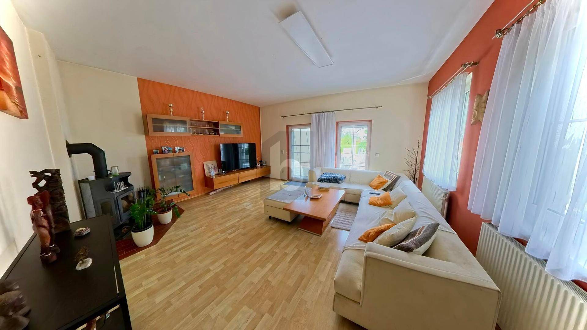 Geräumiges Wohnzimmer mit hellem Parkettboden, orangefarbener Akzentwand und Kaminofen.