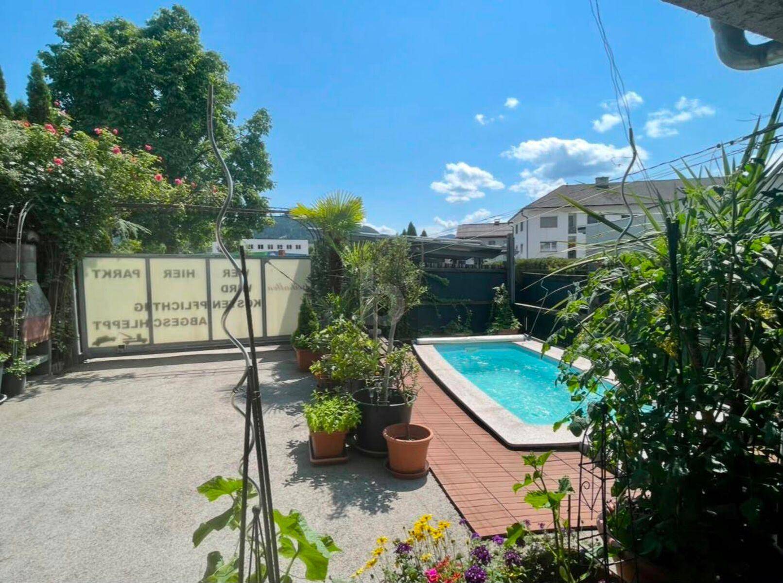 Gartenbereich mit kleinem Pool, umgeben von Topfpflanzen und einer grünen Hecke.