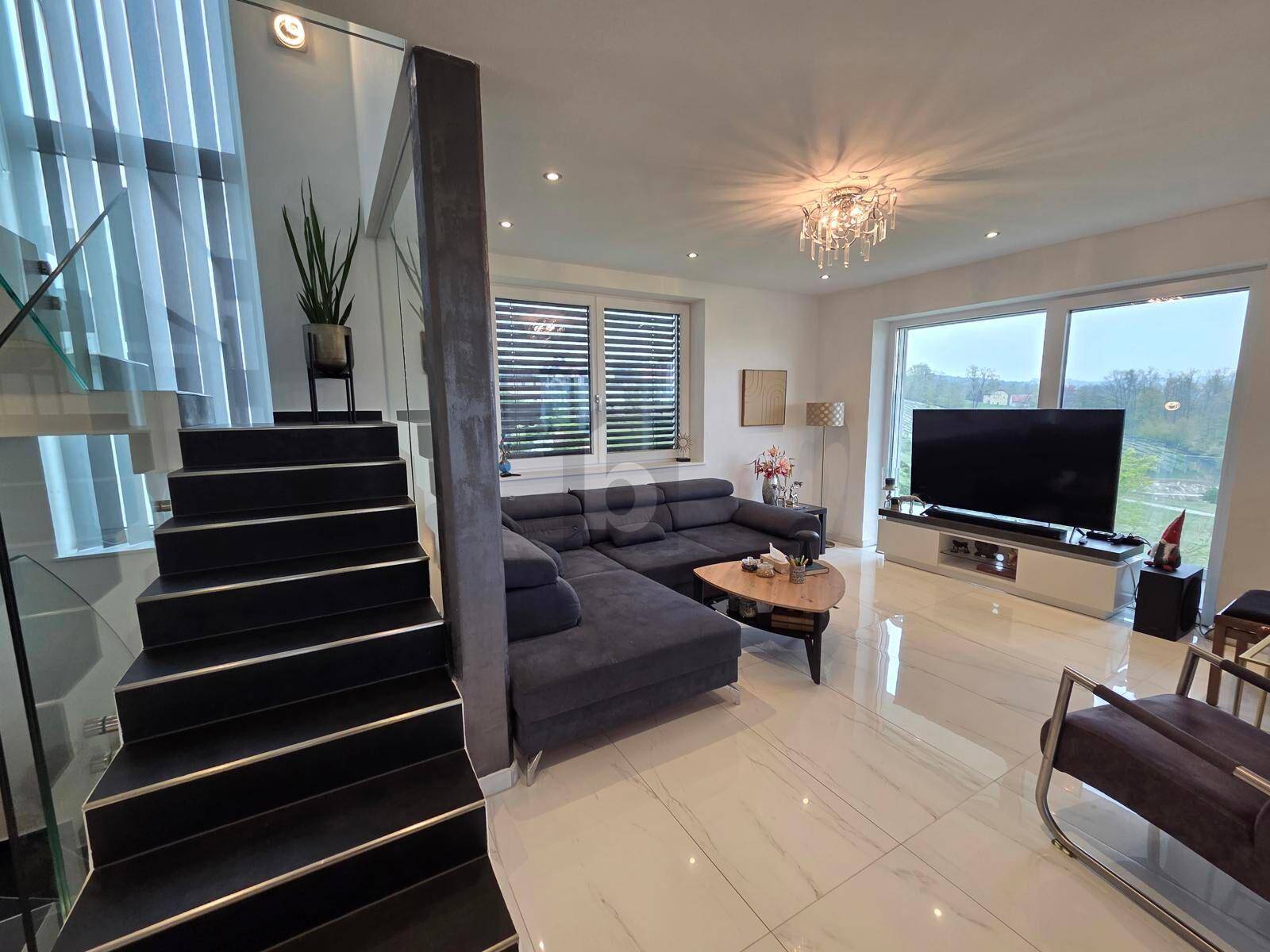 Gemütliches Wohnzimmer mit dunklem Ecksofa, modernen Fliesen und eleganter Treppe mit Glasgeländer.