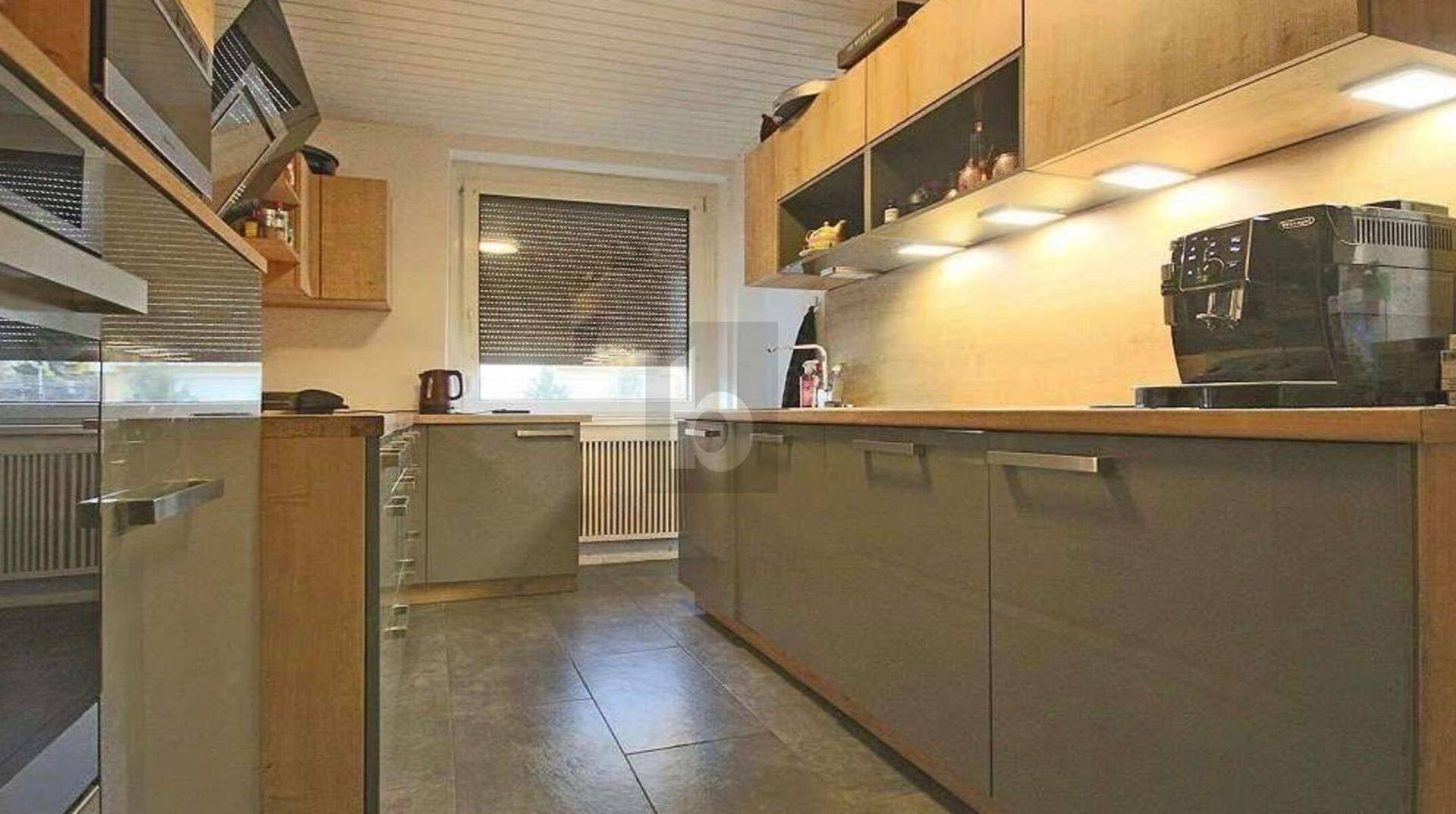 Moderne Küche mit grauen Hochglanzfronten, Holzelementen und integrierten Geräten.