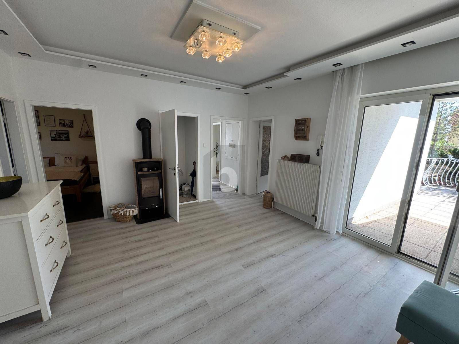Gemütlicher Wohnbereich mit Holzofen, hellem Laminatboden und Zugang zur Terrasse.