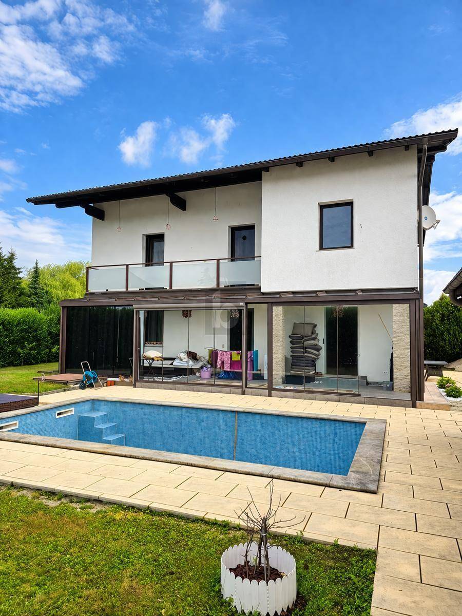 Modernes Haus mit großem Außenpool, gepflegtem Rasen und überdachter Terrasse im Gartenbereich.