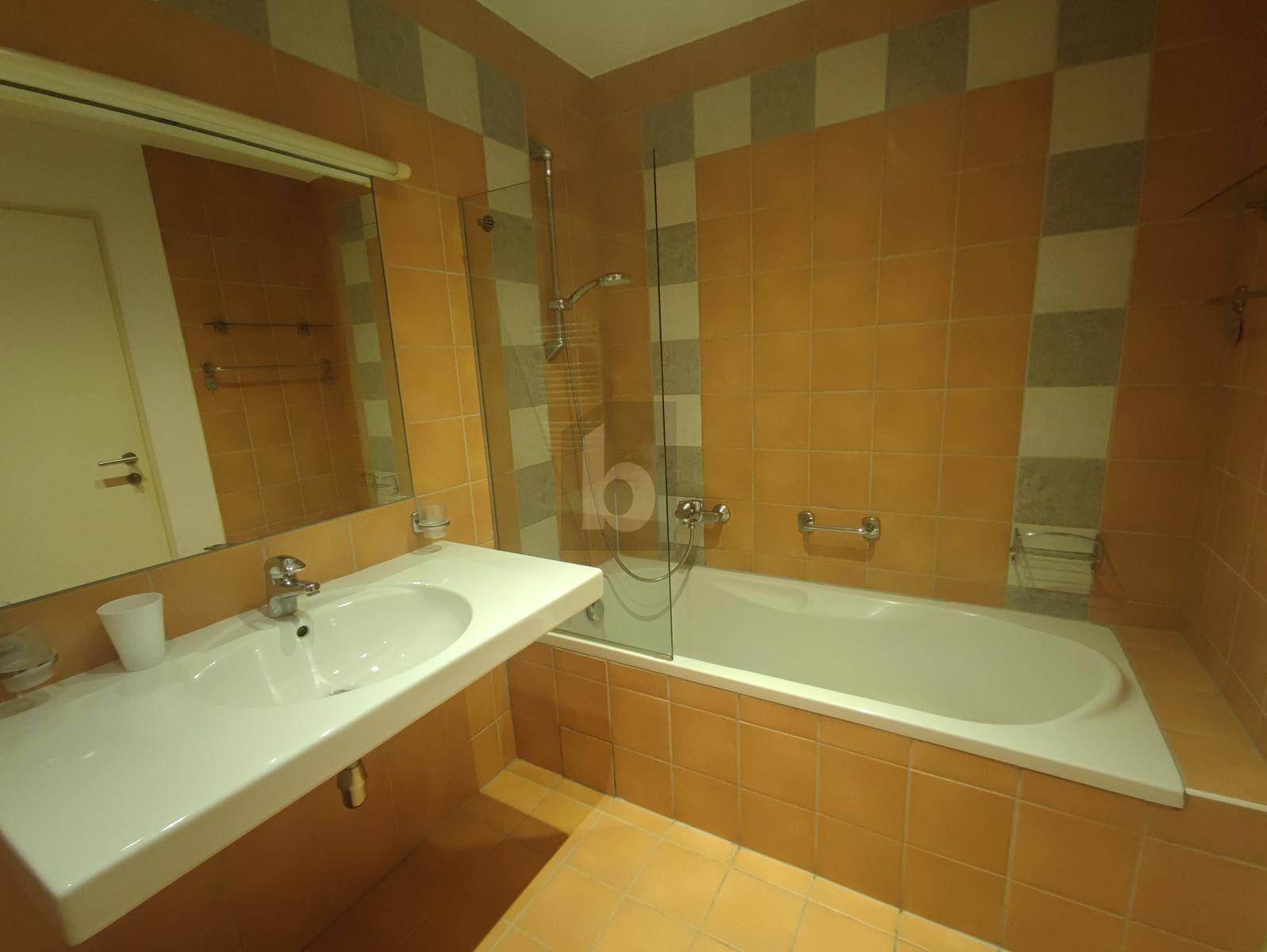Badezimmer mit Badewanne, Duschfunktion und orange-weiß gefliesten Wänden im 80er-Jahre-Stil.