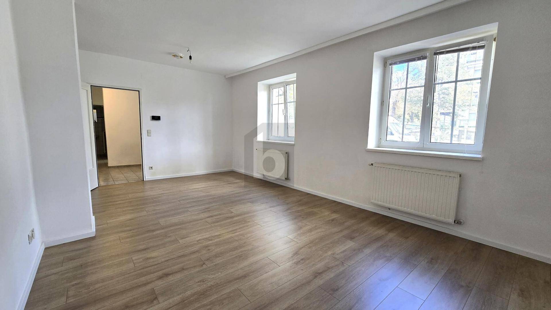 Geräumiges Wohnzimmer mit Laminatboden, weißen Wänden und großen Fenstern für viel Tageslicht.