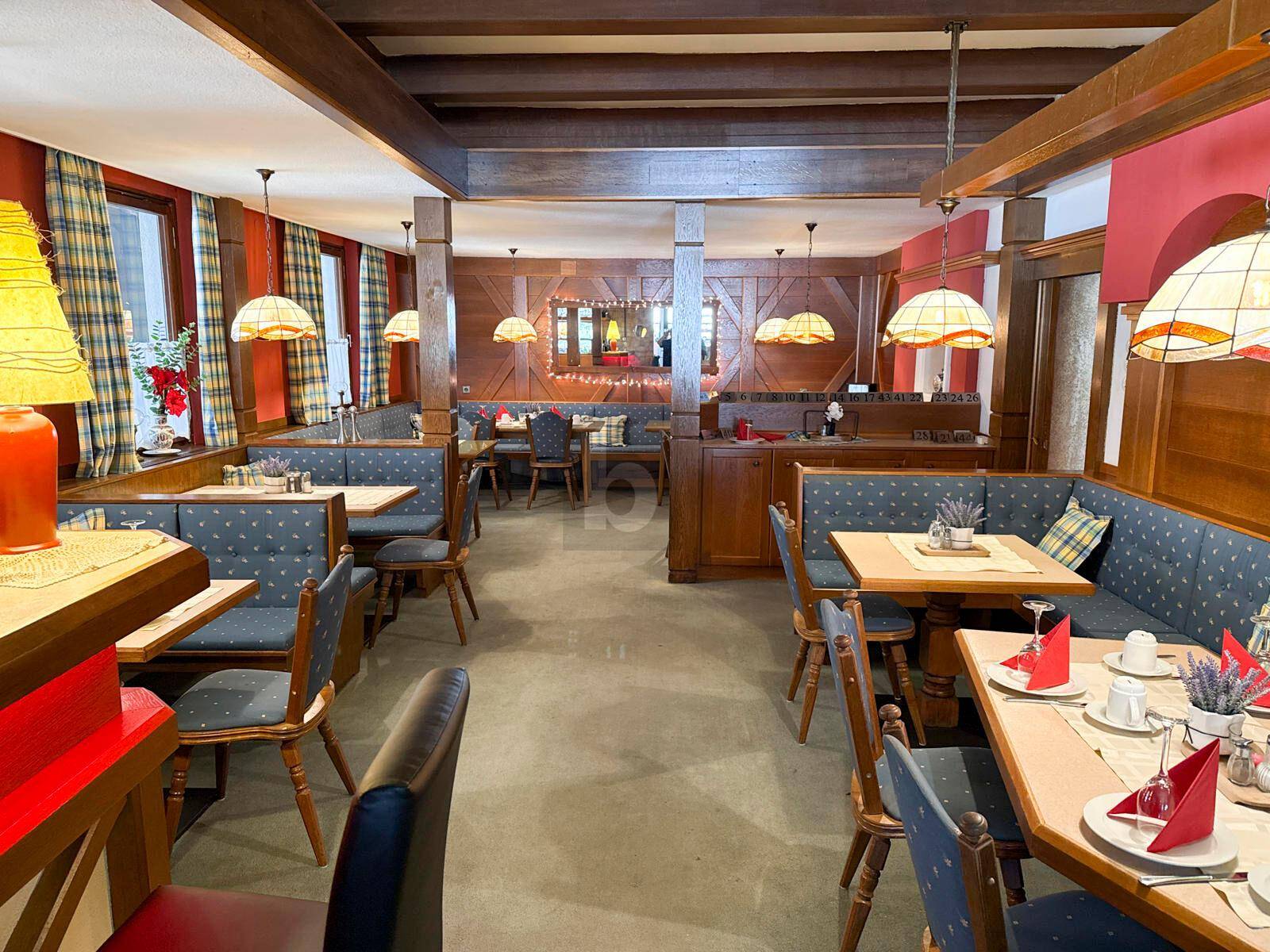 Rustikaler Restaurant-Speisesaal mit Holztischen, blauen Sitzbänken und warmem Licht der Hängelampen.