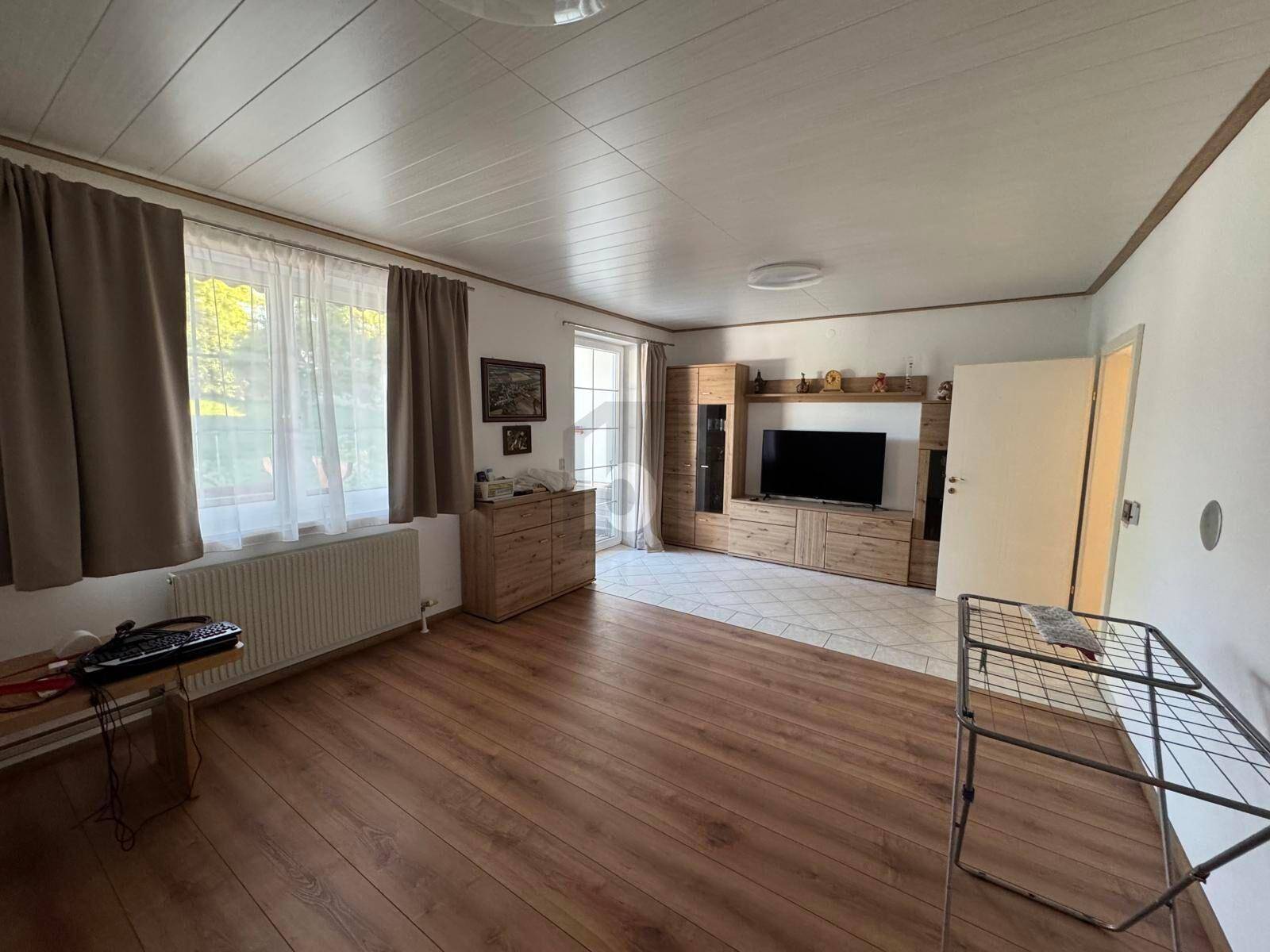 Helles Wohnzimmer mit Laminatboden, großem Fenster und moderner TV-Wand aus Holz.