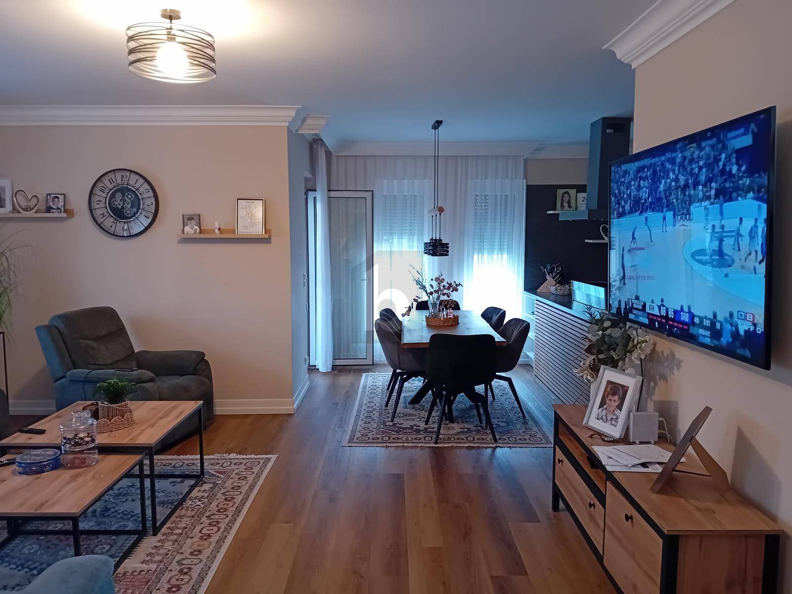 Gemütlicher Wohn-Essbereich mit Holzboden, modernem Mobiliar und einem großen Fernseher.