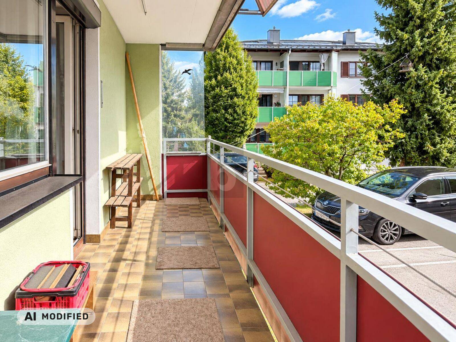 Langer Balkon mit Fliesenboden und Blick auf die umliegenden Gebäude und Parkplätze.