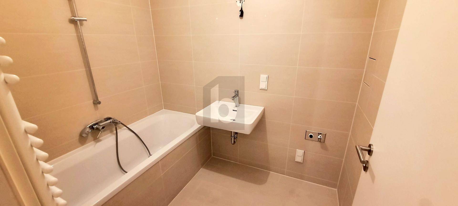 Funktionales Badezimmer mit beigefarbenen Fliesen, Badewanne mit Duschfunktion und Einzelwaschbecken.