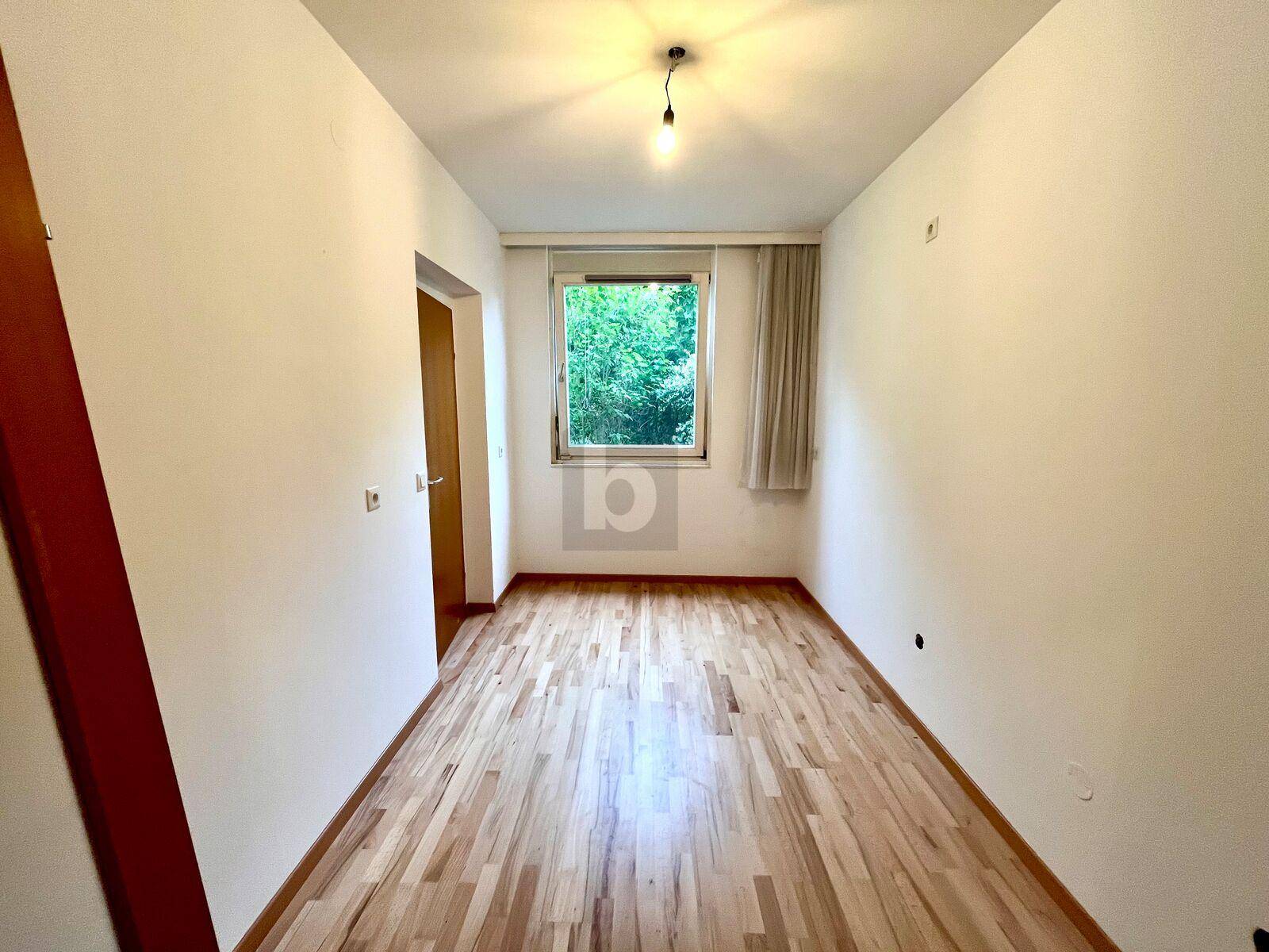 Helles Schlafzimmer mit Parkettboden und einem Fenster, das einen angenehmen Blick ins Grüne bietet.