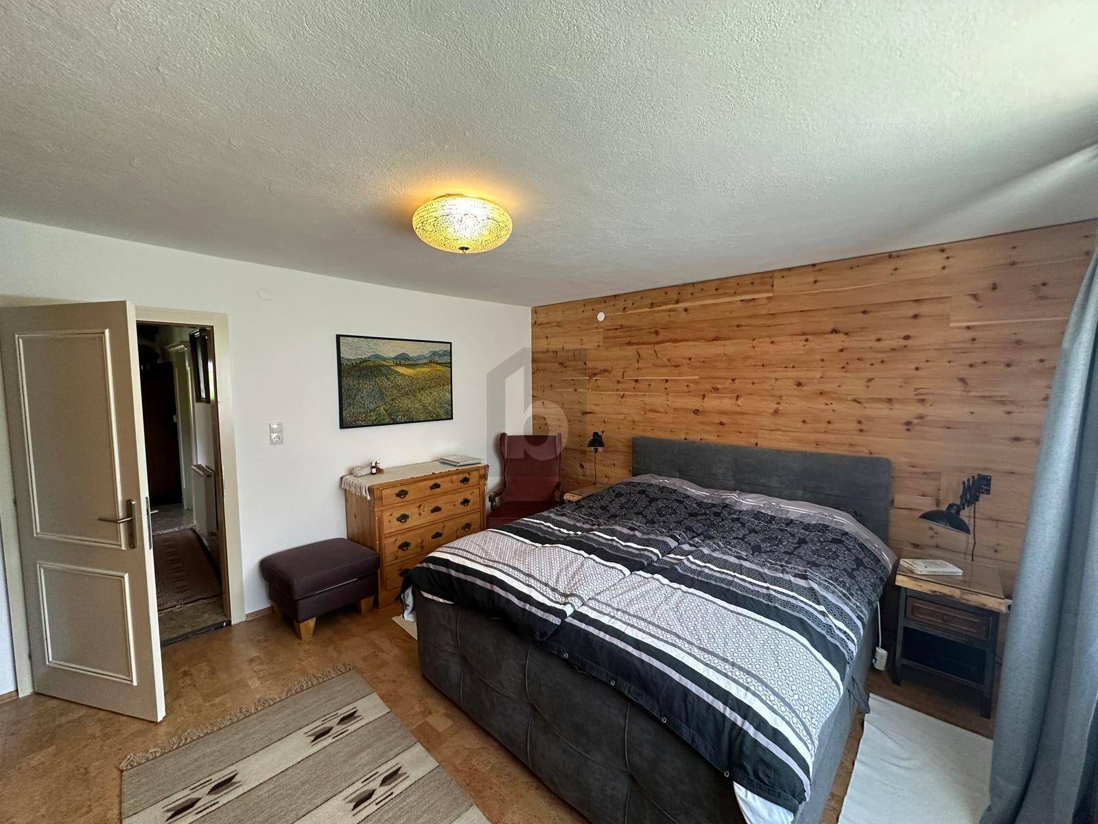 Schlafzimmer mit einer dekorativen Holzwand, Doppelbett und einer klassischen Kommode.