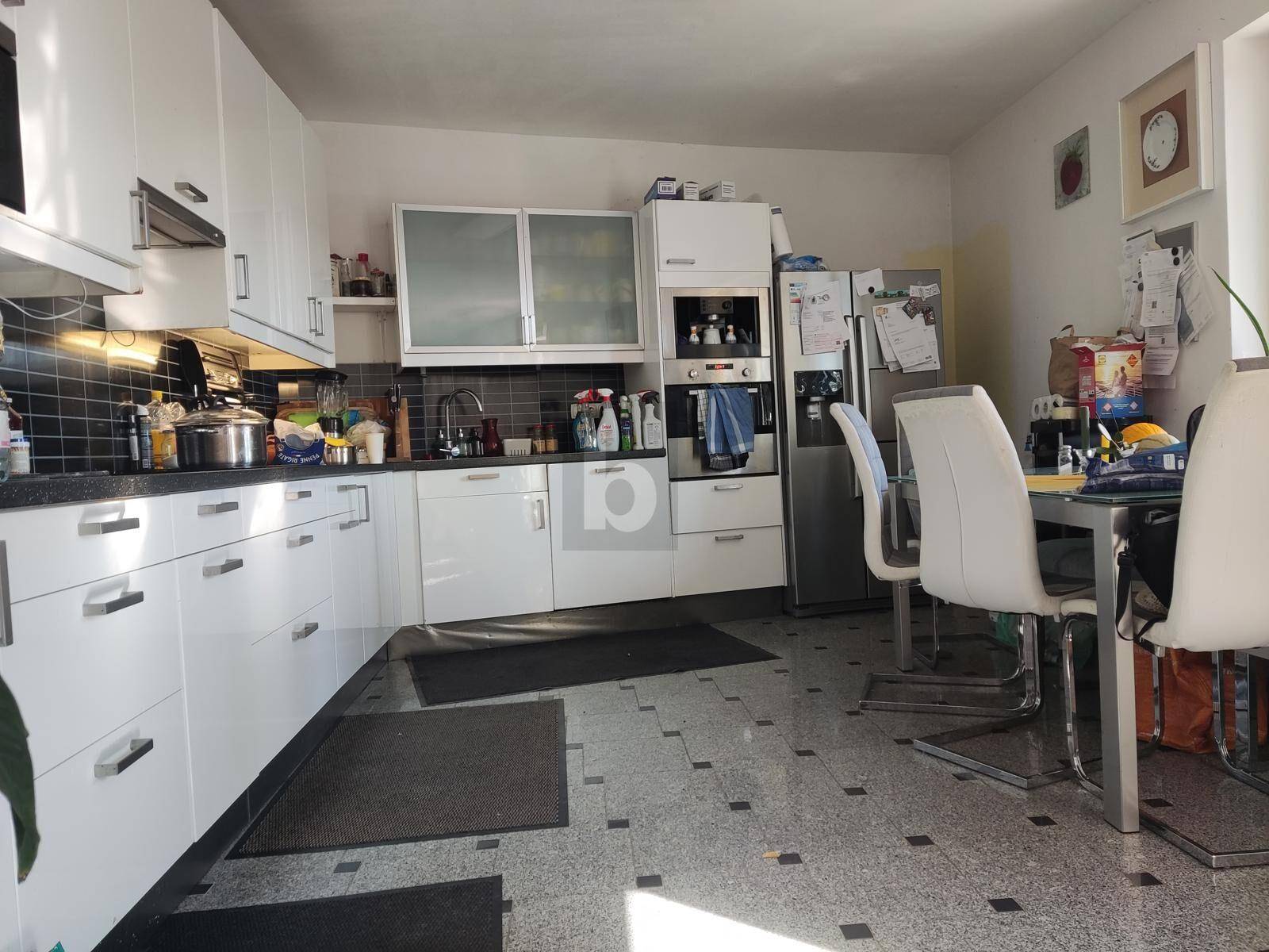 Moderne Küche mit weißen Schränken, einem Essbereich und dunklem Fliesenboden.