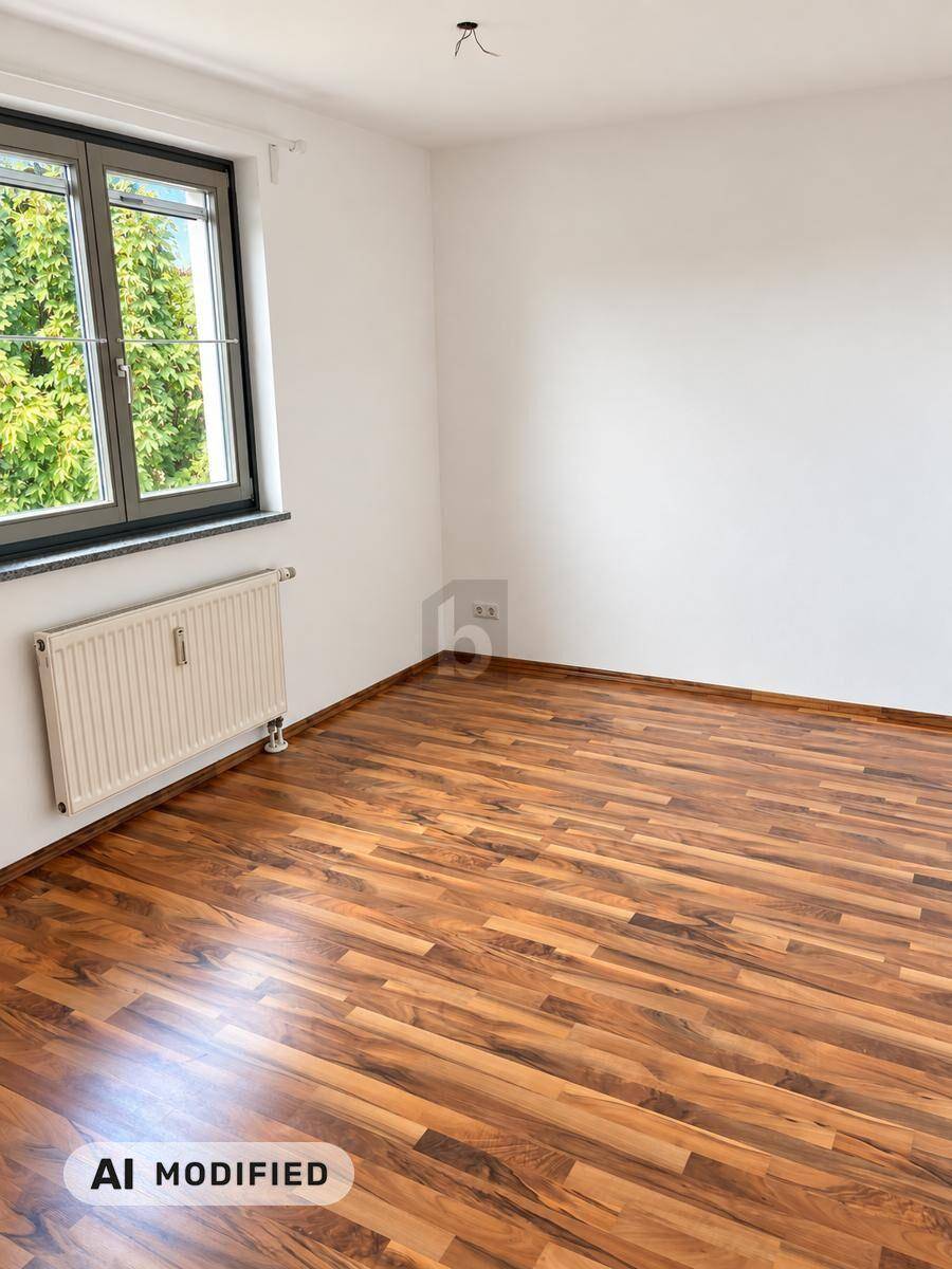 Helles Zimmer mit Laminatboden, weißen Wänden und Fenster mit Blick auf Bäume.