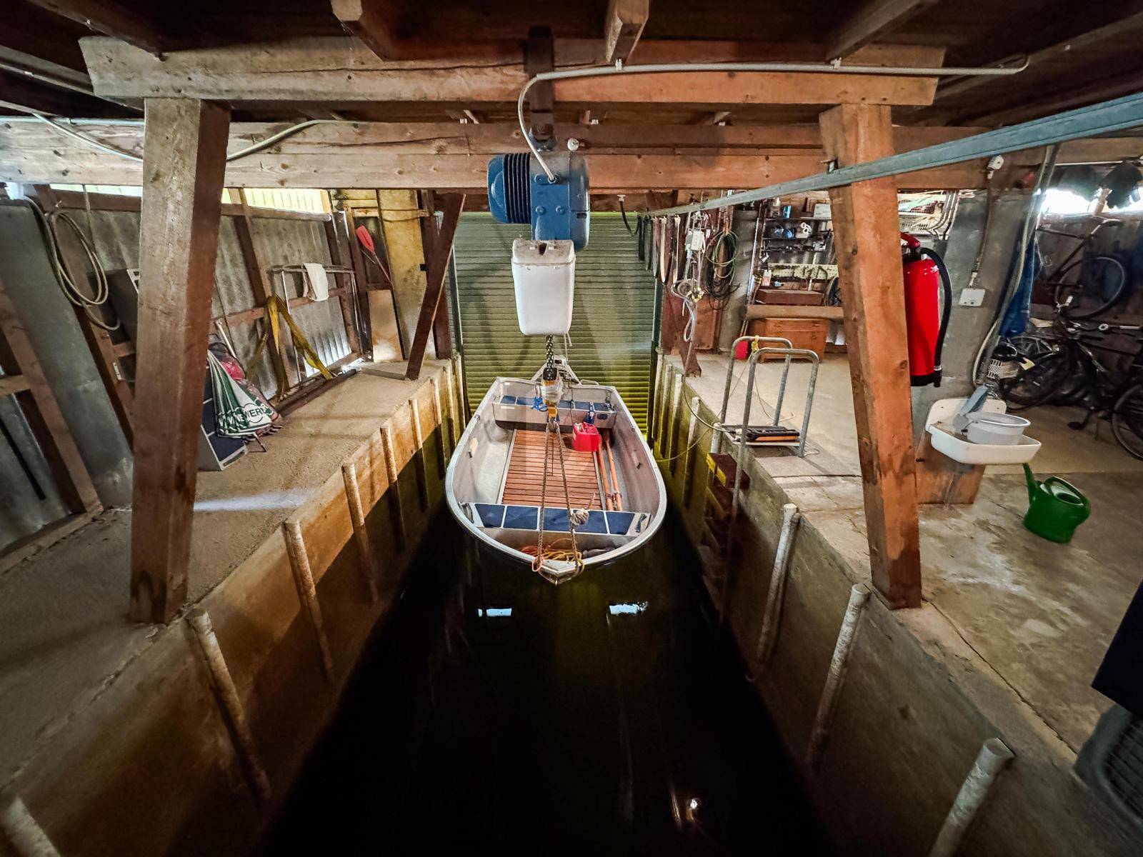 Innenansicht eines Bootshauses mit einem Boot über dem Wasser und sichtbaren Holzkonstruktionen.