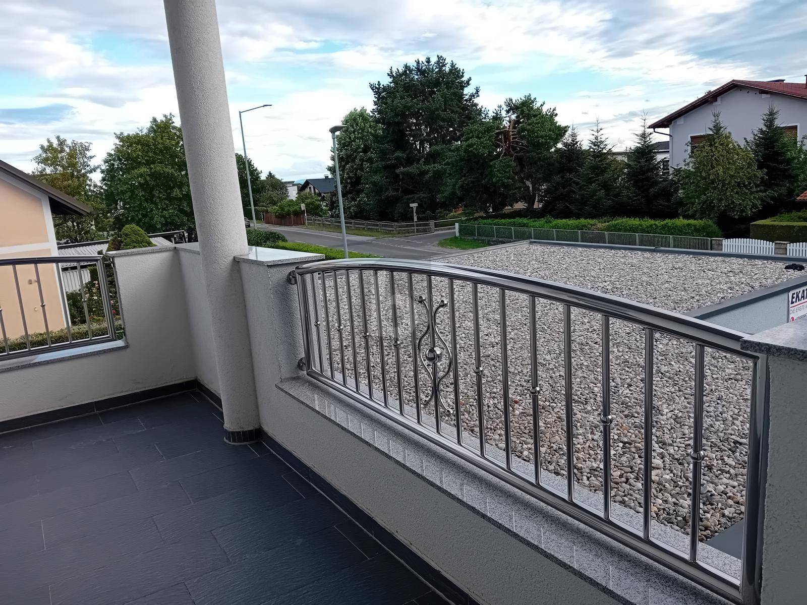 Balkon mit modernem Metallgeländer und Blick auf die Umgebung und eine Kiesfläche.