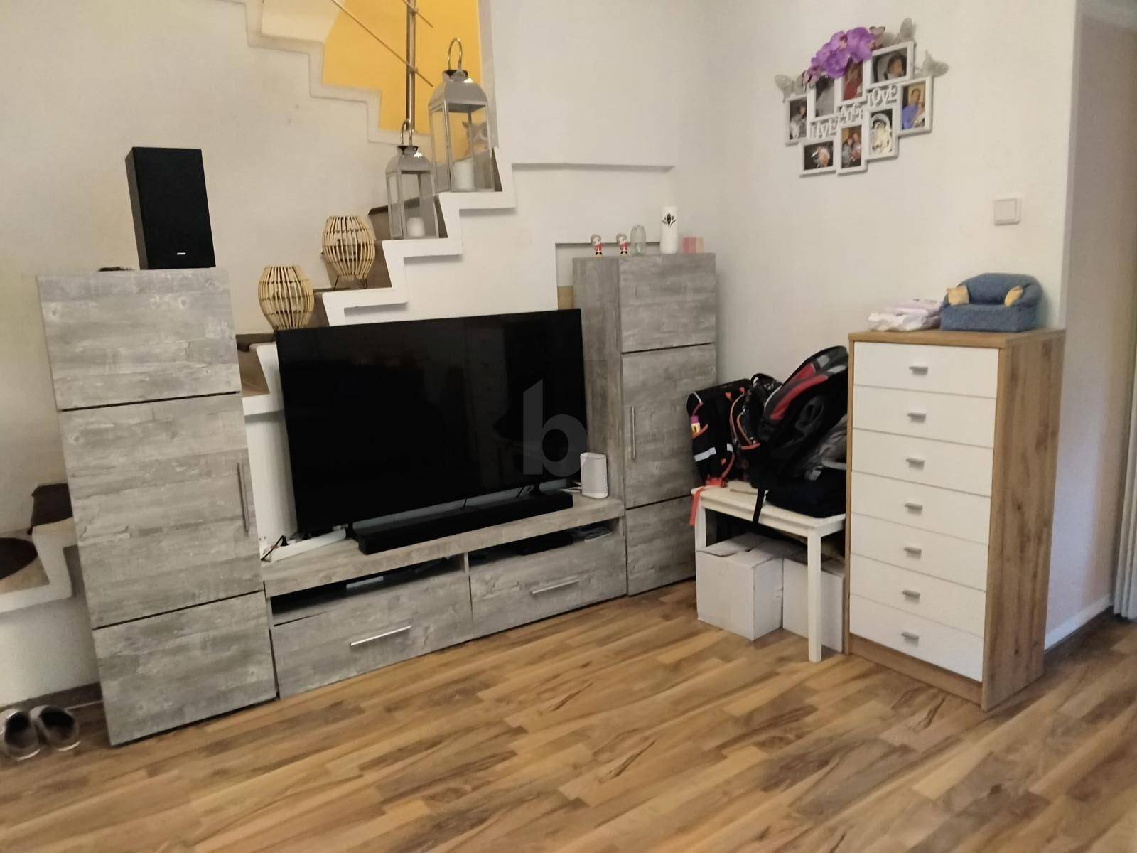 Wohnzimmer mit Laminatboden, moderner TV-Wand und offener Treppe zum Obergeschoss.