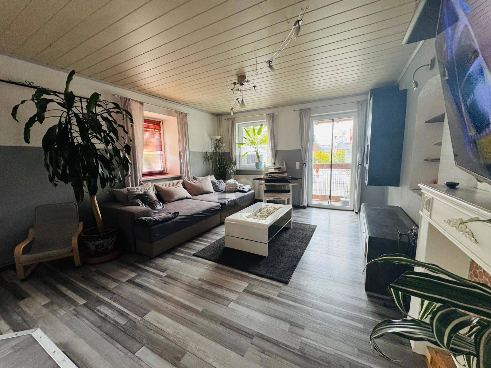 Helles Wohnzimmer mit Laminatboden, bequemer Couch und Zugang zum Balkon.