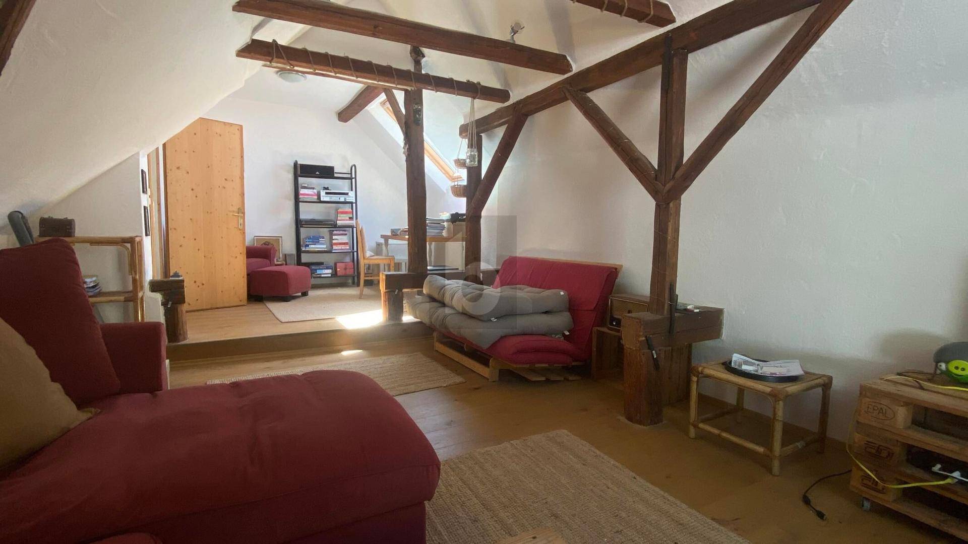 Gemütlicher Wohnbereich im Dachgeschoss mit sichtbaren Holzbalken und schrägen Decken.