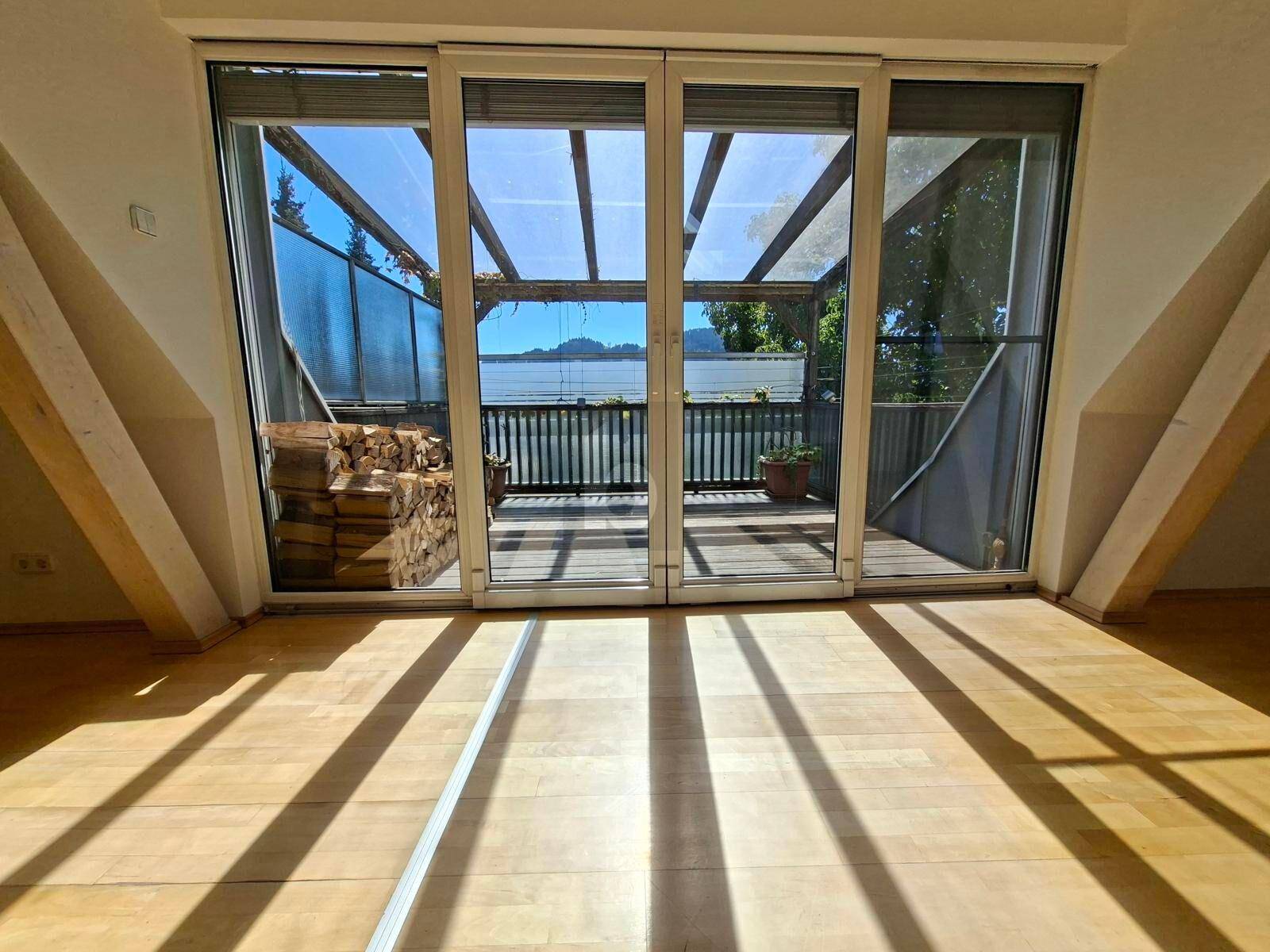 Heller Innenraum mit Holzboden und großen Schiebetüren, die zu einem Balkon mit Seeblick führen.