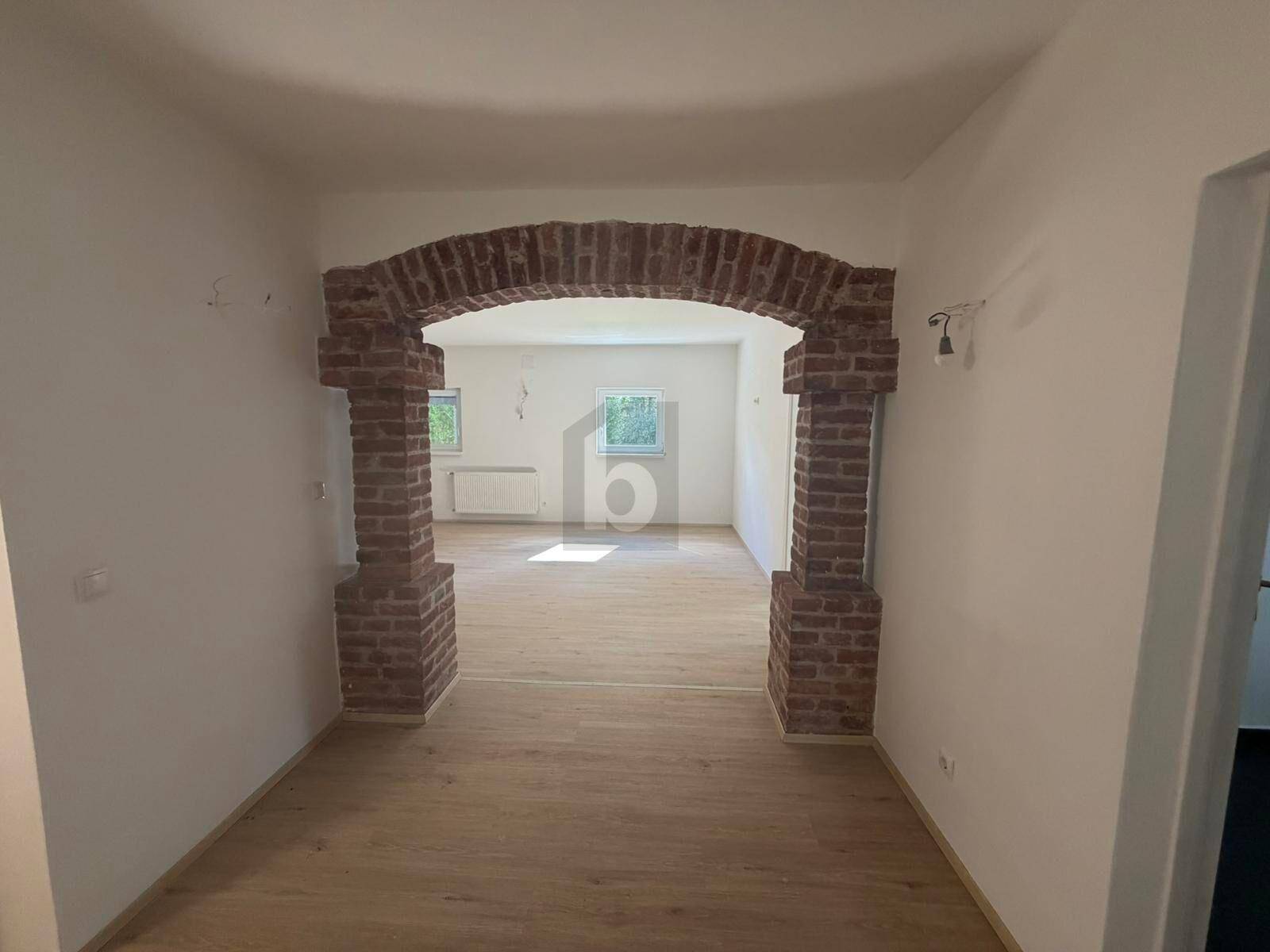 Heller Flur mit dekorativem Ziegelbogen, der zu einem weiteren Raum mit Holzboden führt.