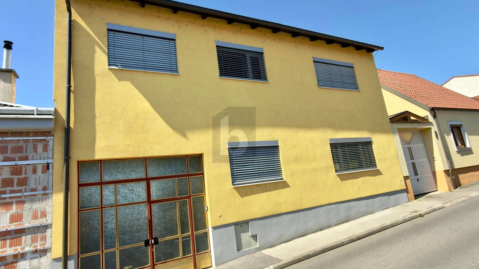 Gelbe Hausfassade mit Garagentor und Rollläden an den Fenstern.