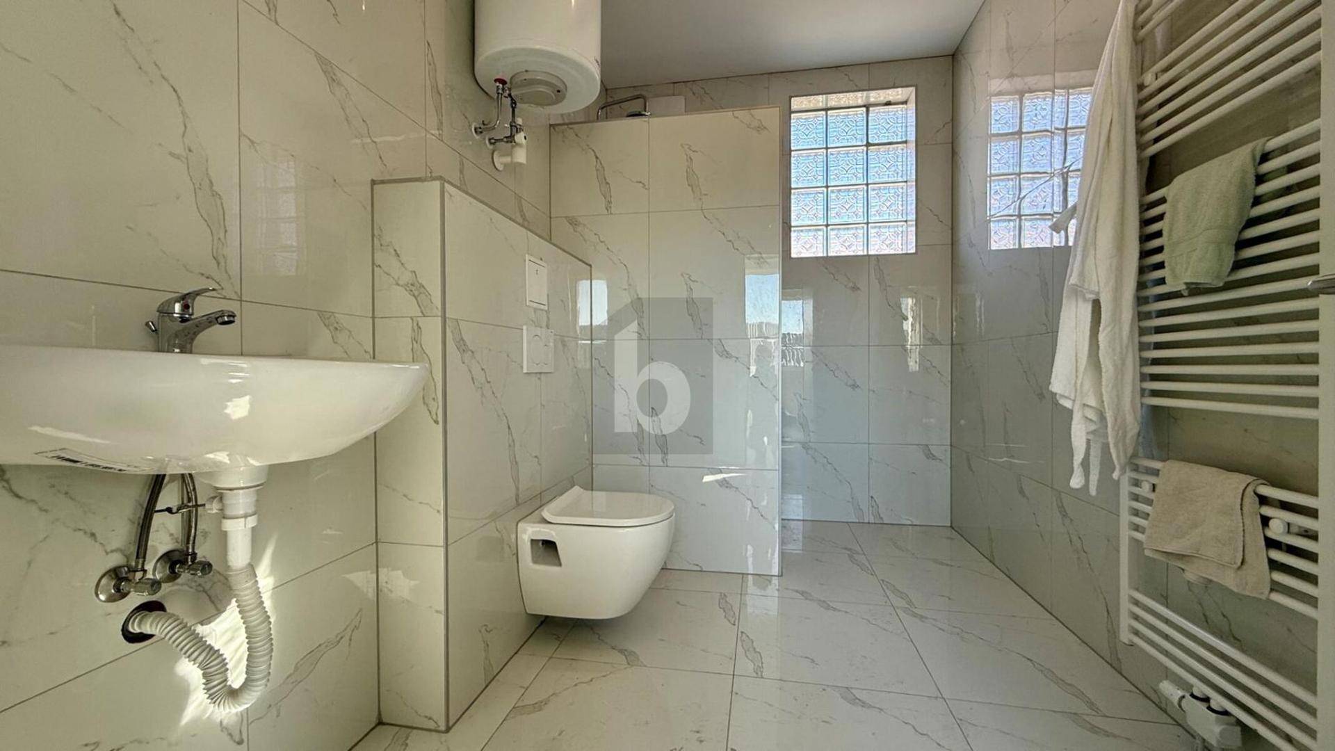 Modernes Badezimmer mit Marmorfliesen, wandhängendem WC, Waschbecken und Handtuchheizkörper.