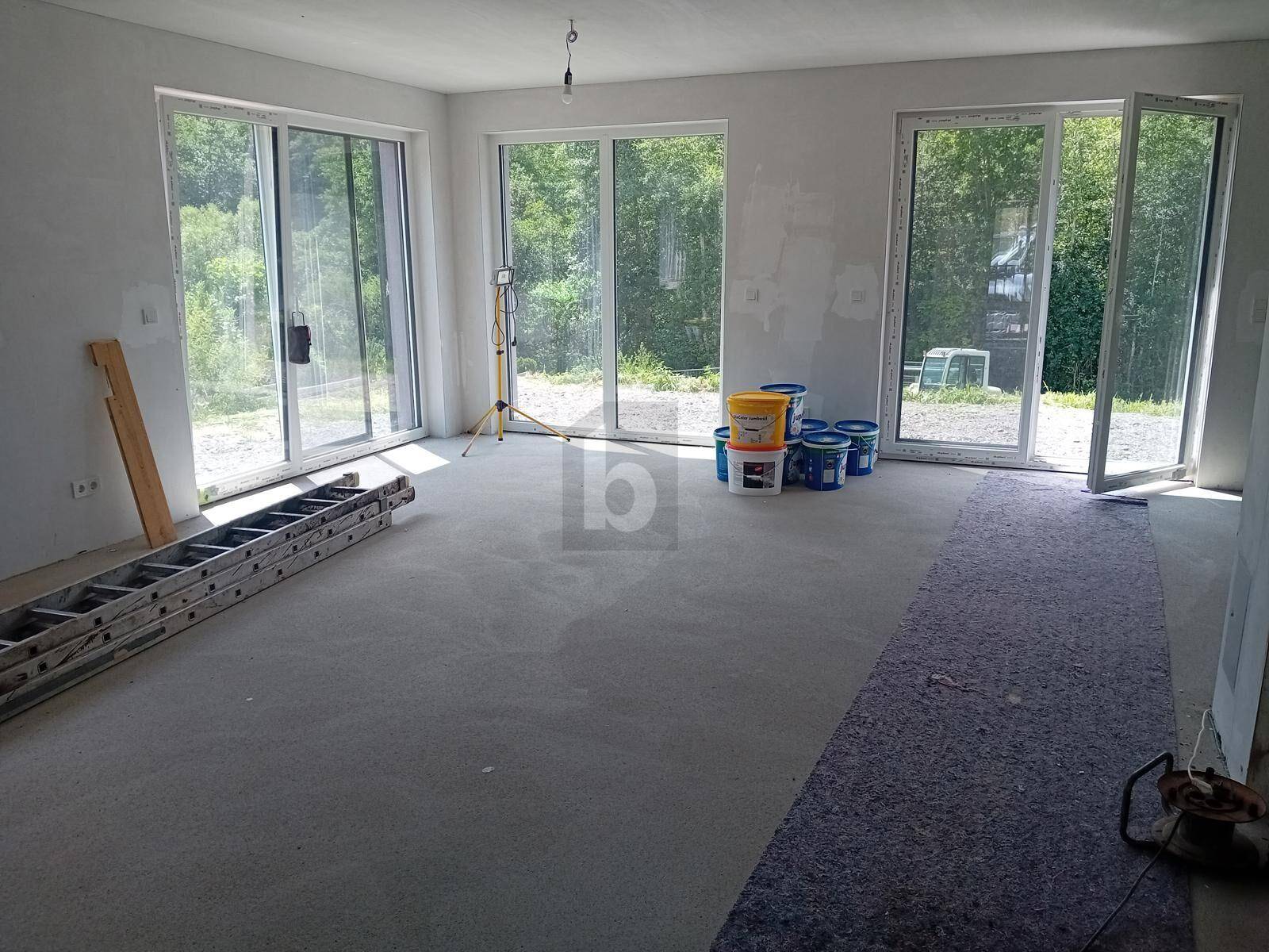 Unfertiger Wohnraum mit großen Schiebetüren, die viel Tageslicht hereinlassen und Blick ins Grüne bieten.