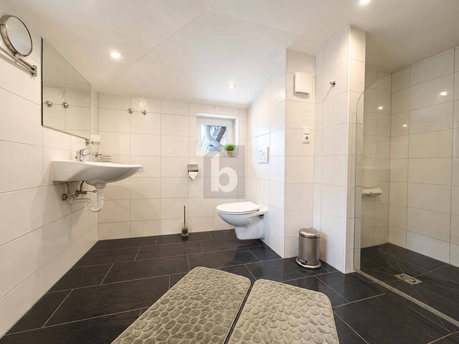 Modernes Badezimmer mit weißen Fliesen, dunklem Boden, wandhängendem WC und begehbarer Dusche.