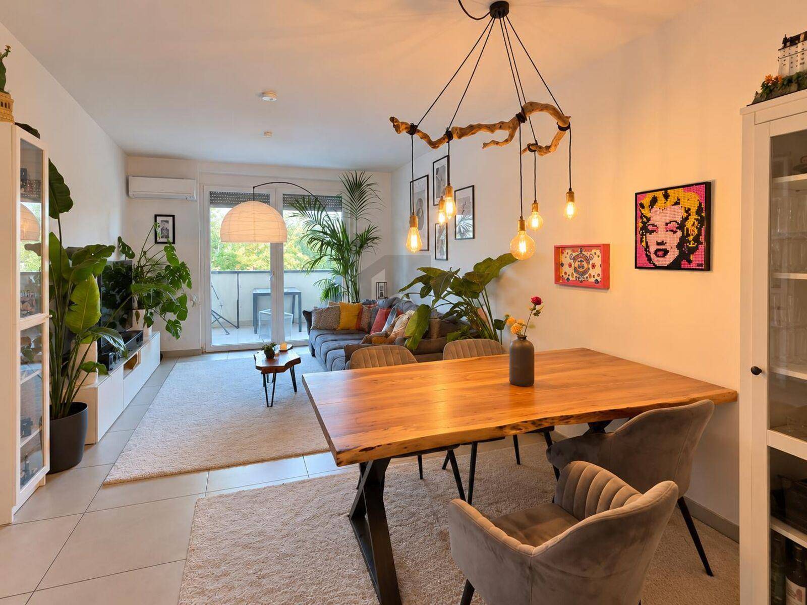 Moderner offener Wohn-Essbereich mit Holztisch, bequemen Stühlen und Zugang zum Balkon, umgeben von Pflanzen.