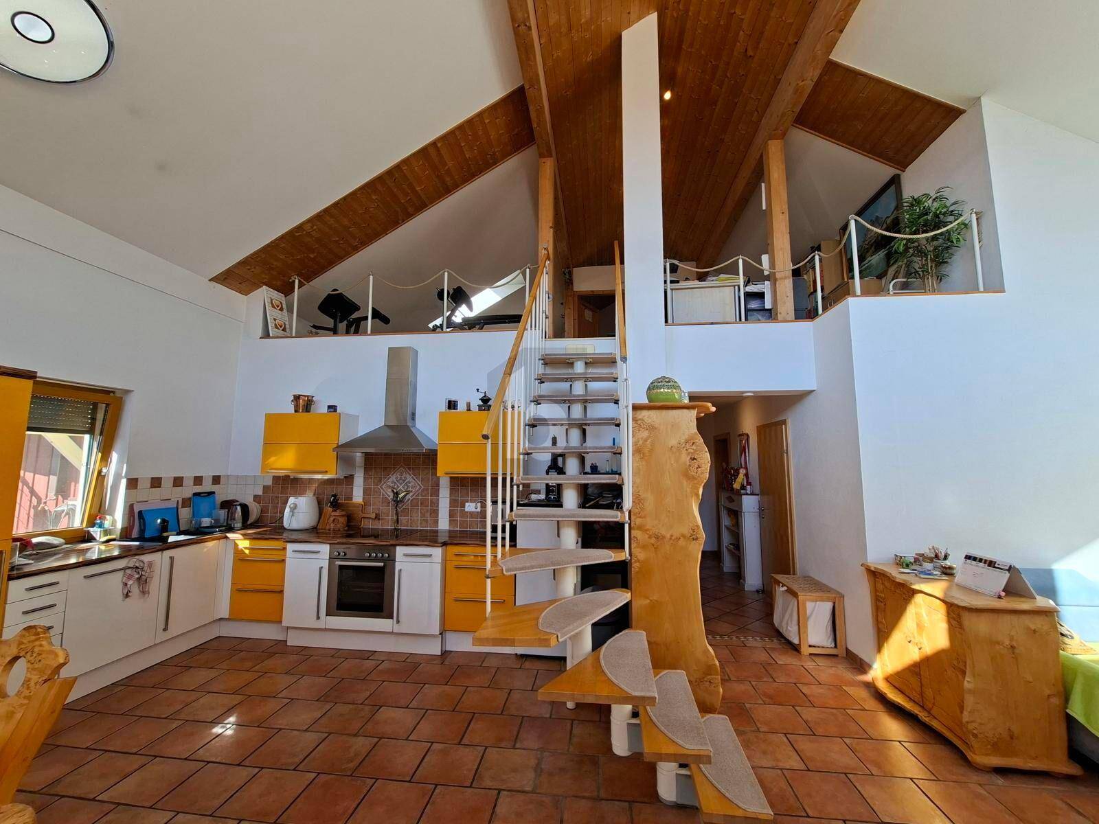 Offene Küche mit gelben Schränken, Holzdecke und einer Wendeltreppe, die zu einer Galerie führt.