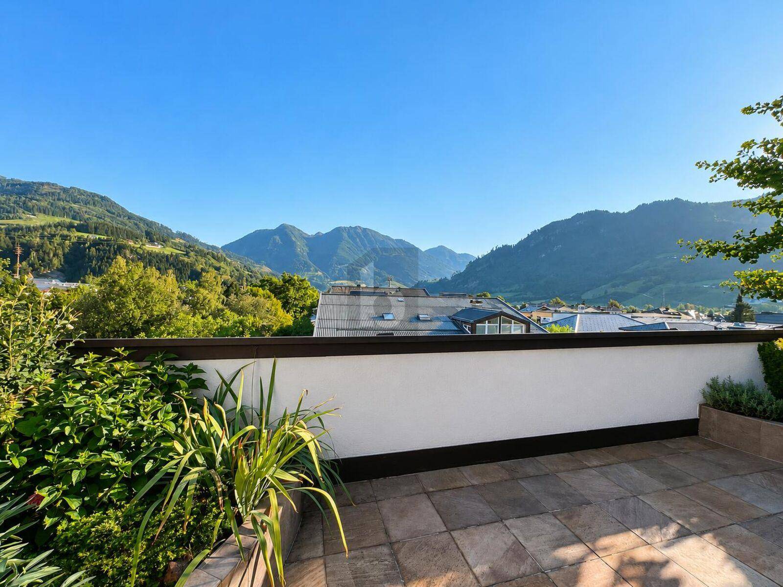 Geräumige Terrasse mit Fliesenboden und üppiger Bepflanzung, die einen weiten Blick auf die umliegenden Berge bietet.