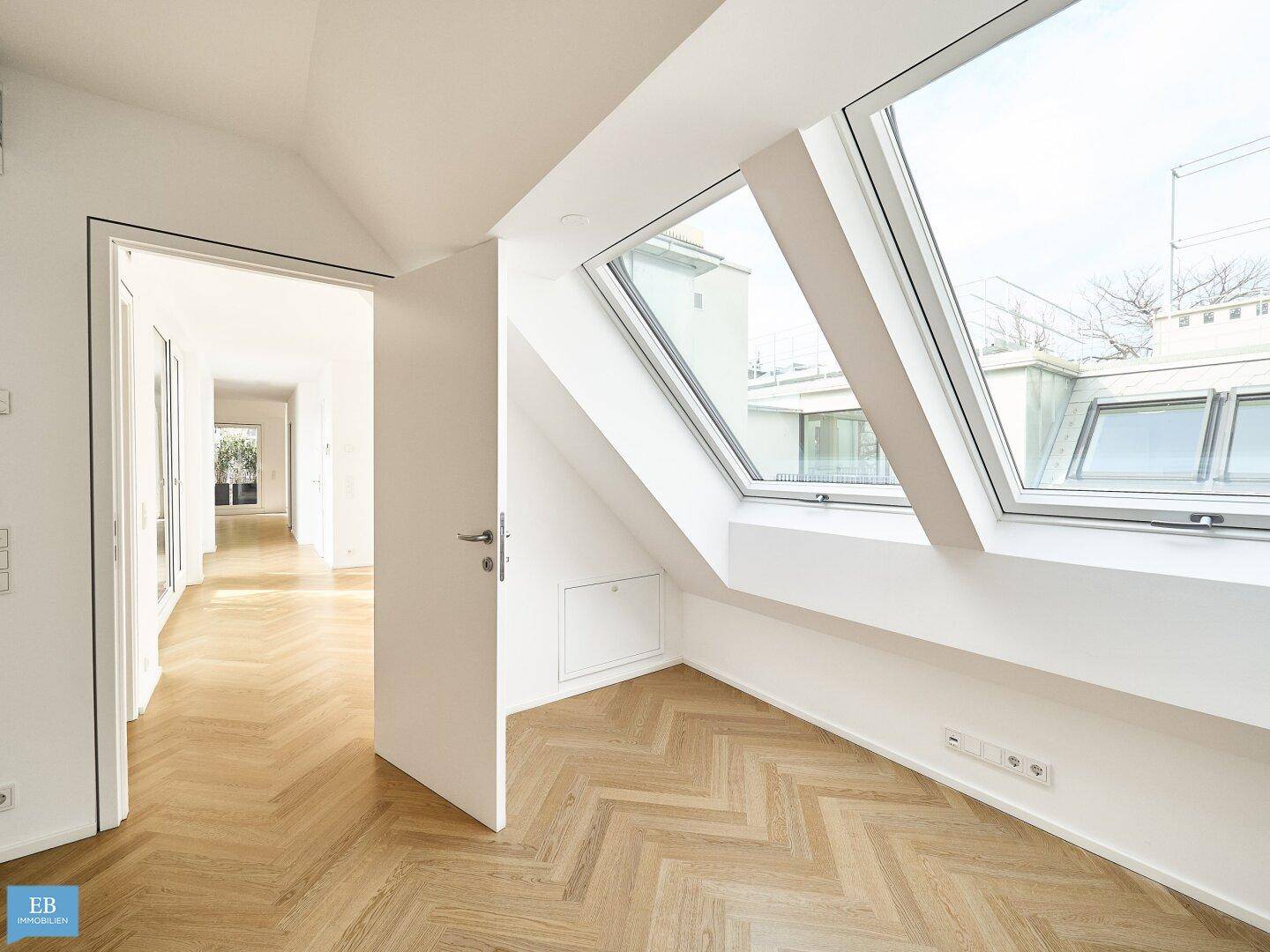 Geräumiges Zimmer im Dachgeschoss mit schrägen Wänden, großen Dachfenstern und Fischgrätparkett.