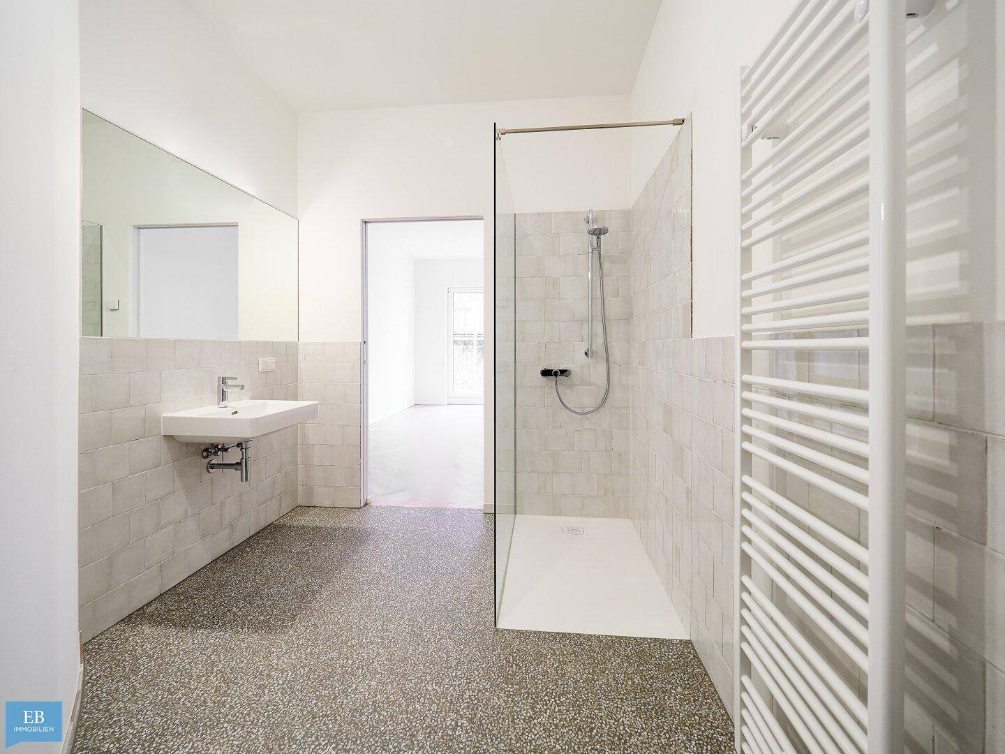 Helles Badezimmer mit ebenerdiger Dusche, Waschbecken und großem Spiegel, das einen modernen Eindruck vermittelt.