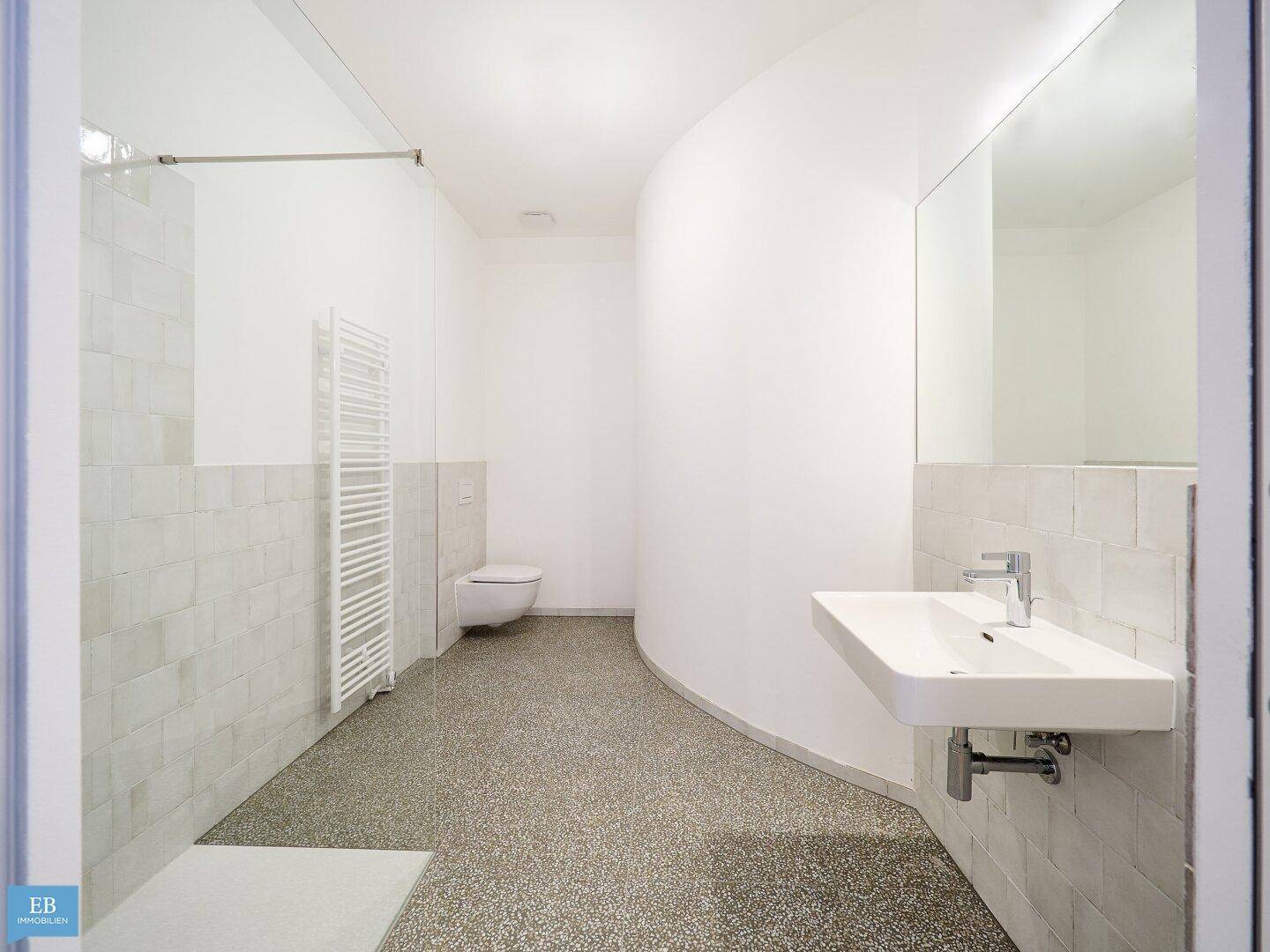 Geräumiges Badezimmer mit moderner Wandtoilette, Waschbecken und großer Spiegelfläche für Komfort.