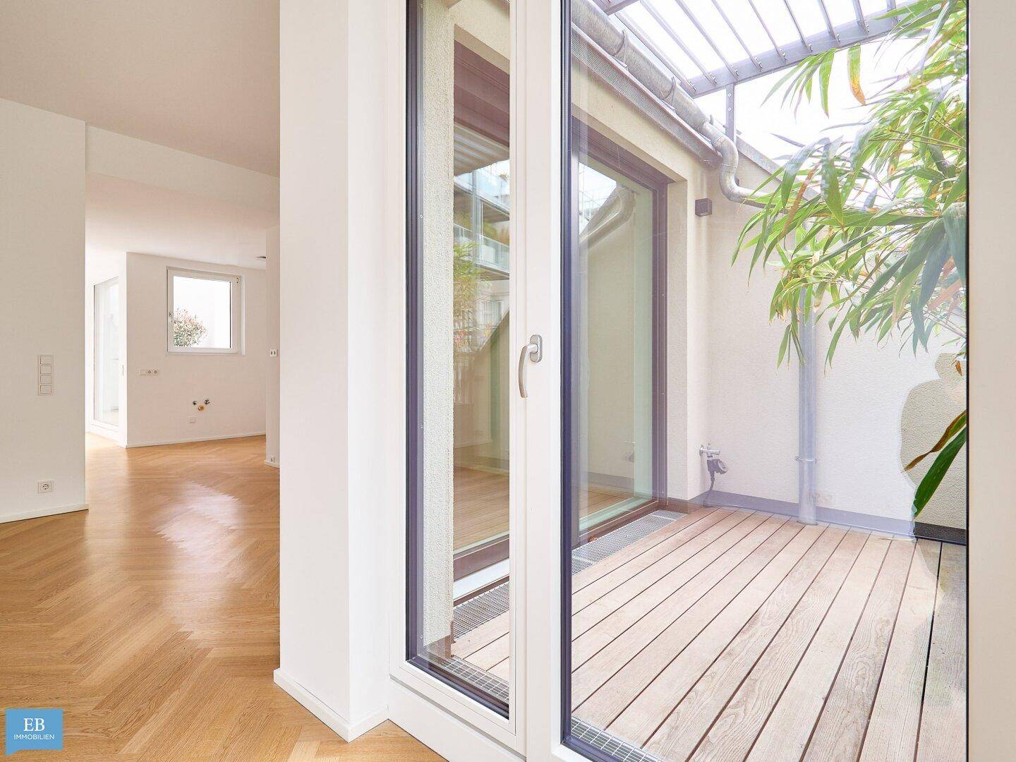 Heller Wohnbereich mit Holzboden und großen Glasfronten, die den Blick auf die begrünte Terrasse freigeben.