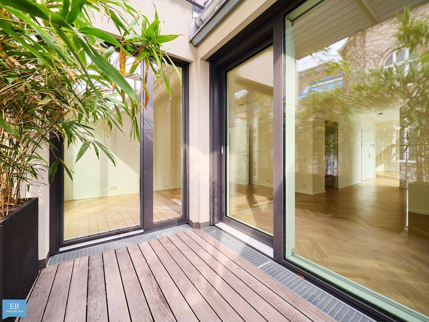 Helle Terrasse mit Holzboden, großen Schiebetüren und üppiger Bepflanzung in modernen Pflanzkübeln.