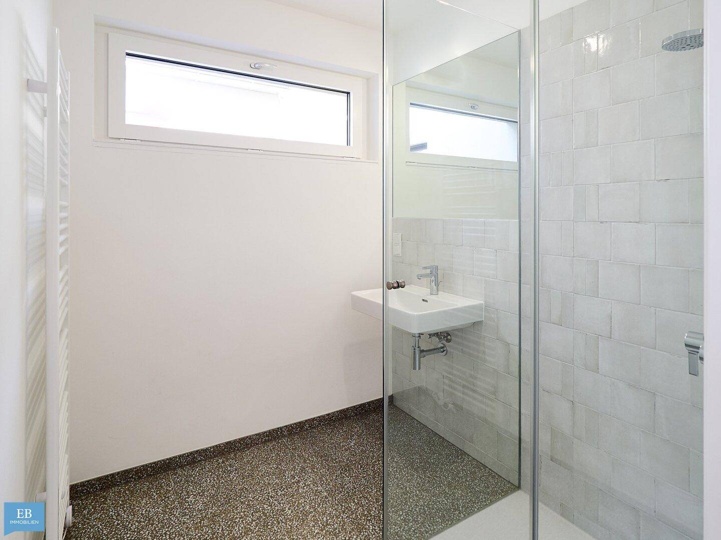 Modernes Badezimmer mit ebenerdiger Dusche, Fenster und einem praktischen beheizten Handtuchhalter.