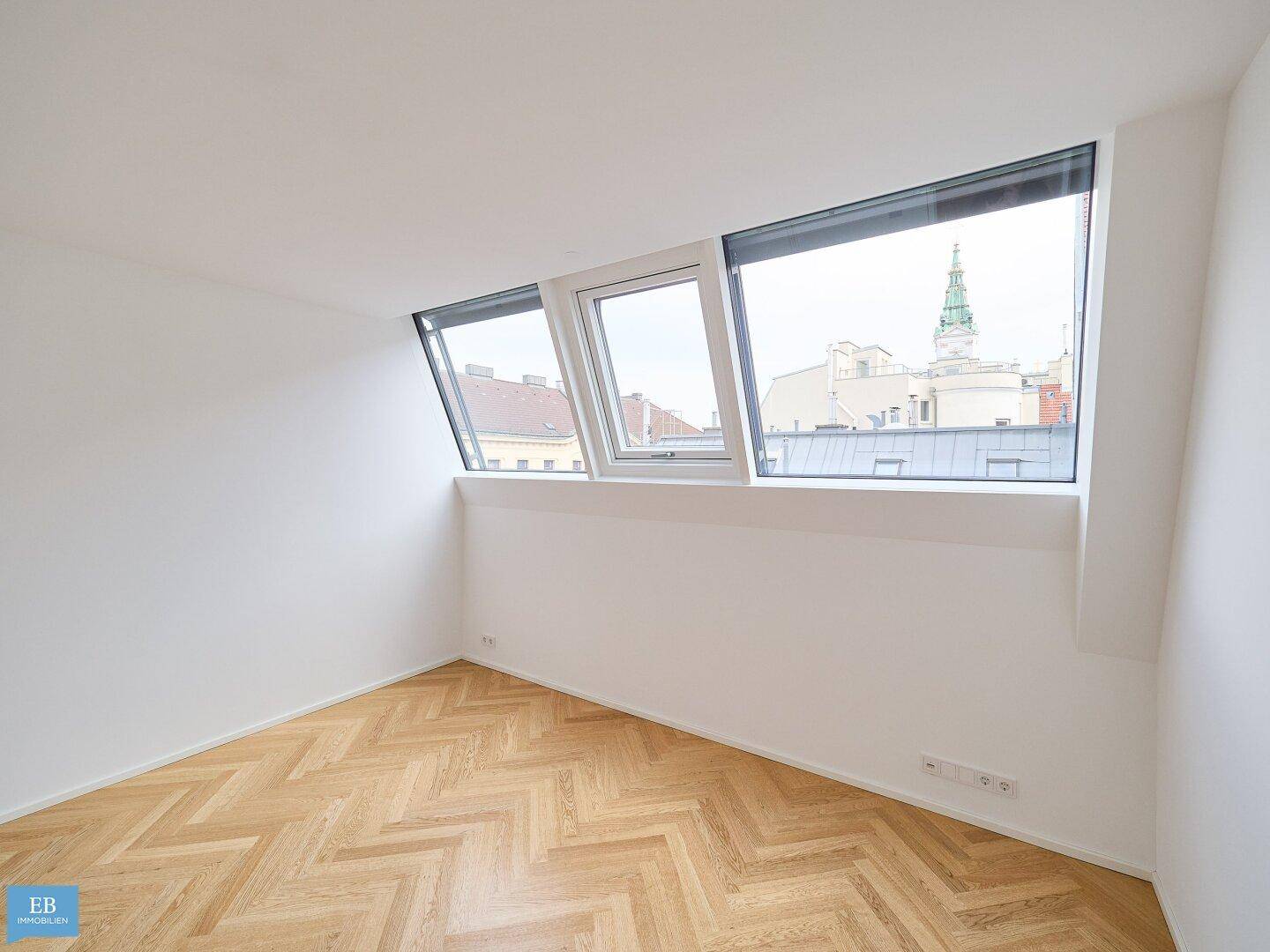 Helles Zimmer mit Fischgrätparkett, weißen Wänden und modernen Dachfenstern mit Stadtblick.