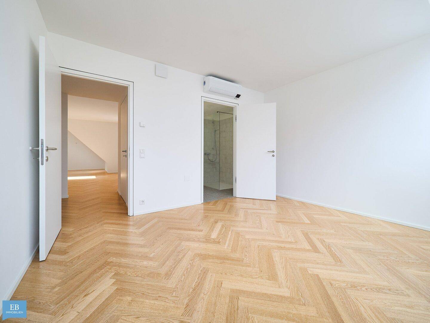 Geräumiges Zimmer mit Fischgrätparkett, Klimaanlage und direktem Zugang zu einem Badezimmer mit Dusche.