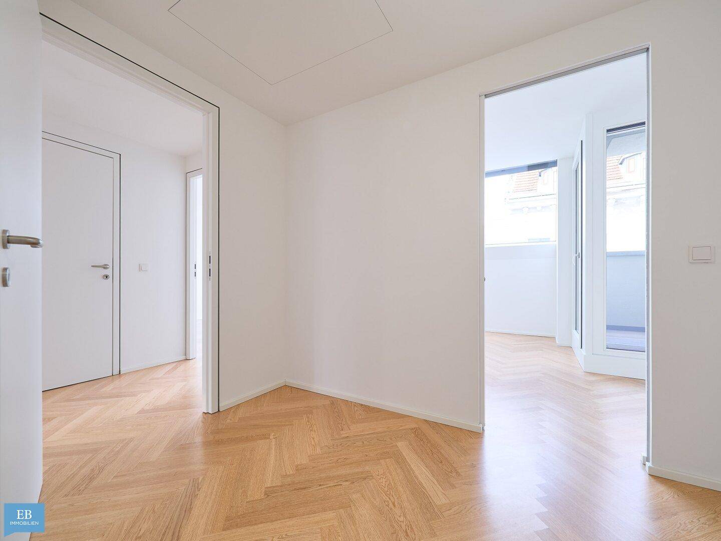 Geräumiger Flur mit Fischgrätparkett und Zugang zu verschiedenen Zimmern, eines davon mit Balkon.