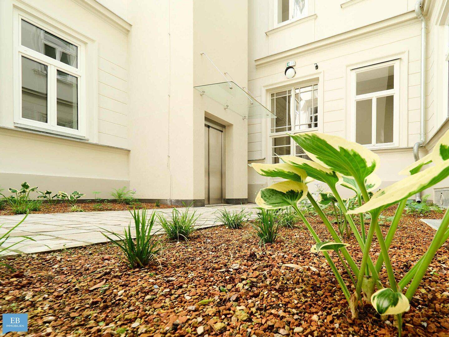 Kleiner, gepflegter Gartenbereich im Innenhof mit jungen Pflanzen und einem Aufzug.