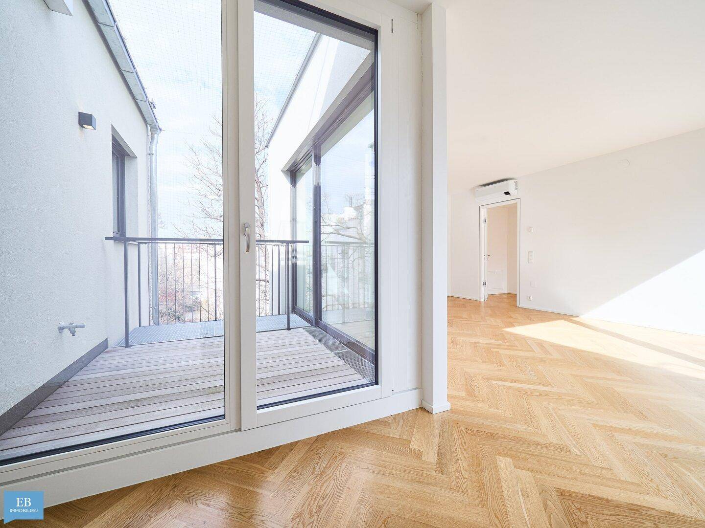 Heller Wohnbereich mit Fischgrätparkett und Zugang zu einem kleinen Balkon, lichtdurchflutet.