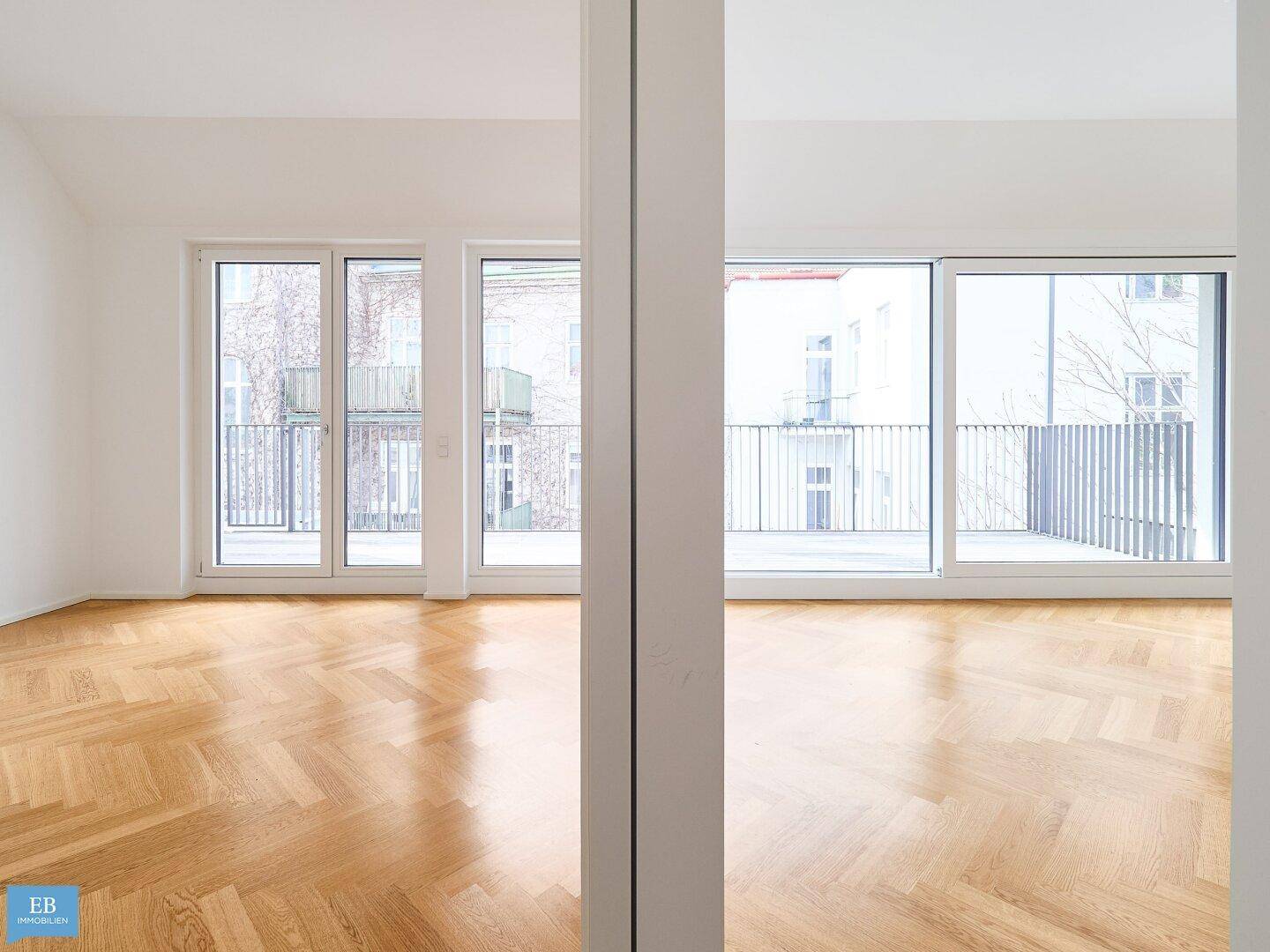 Offener Wohnbereich mit hellem Fischgrätparkett und breiten Fensterfronten, die viel Licht hereinlassen.