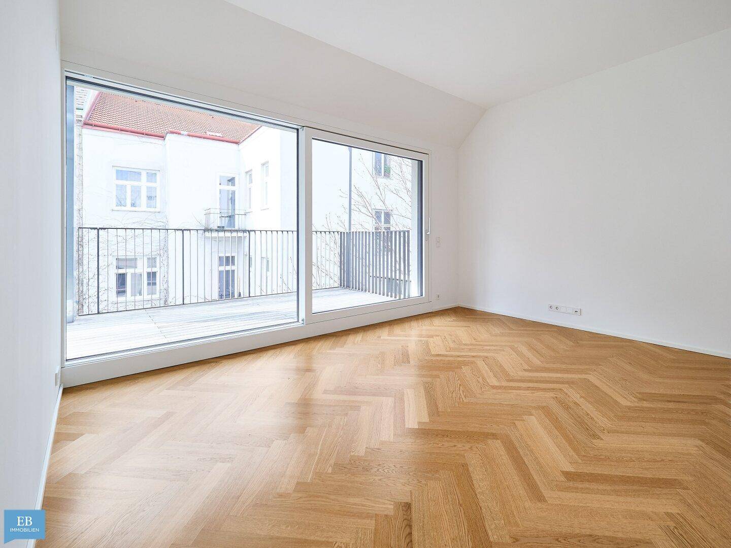 Lichtdurchfluteter Wohnraum mit Fischgrätparkett und großzügigen Schiebetüren zum Balkon.