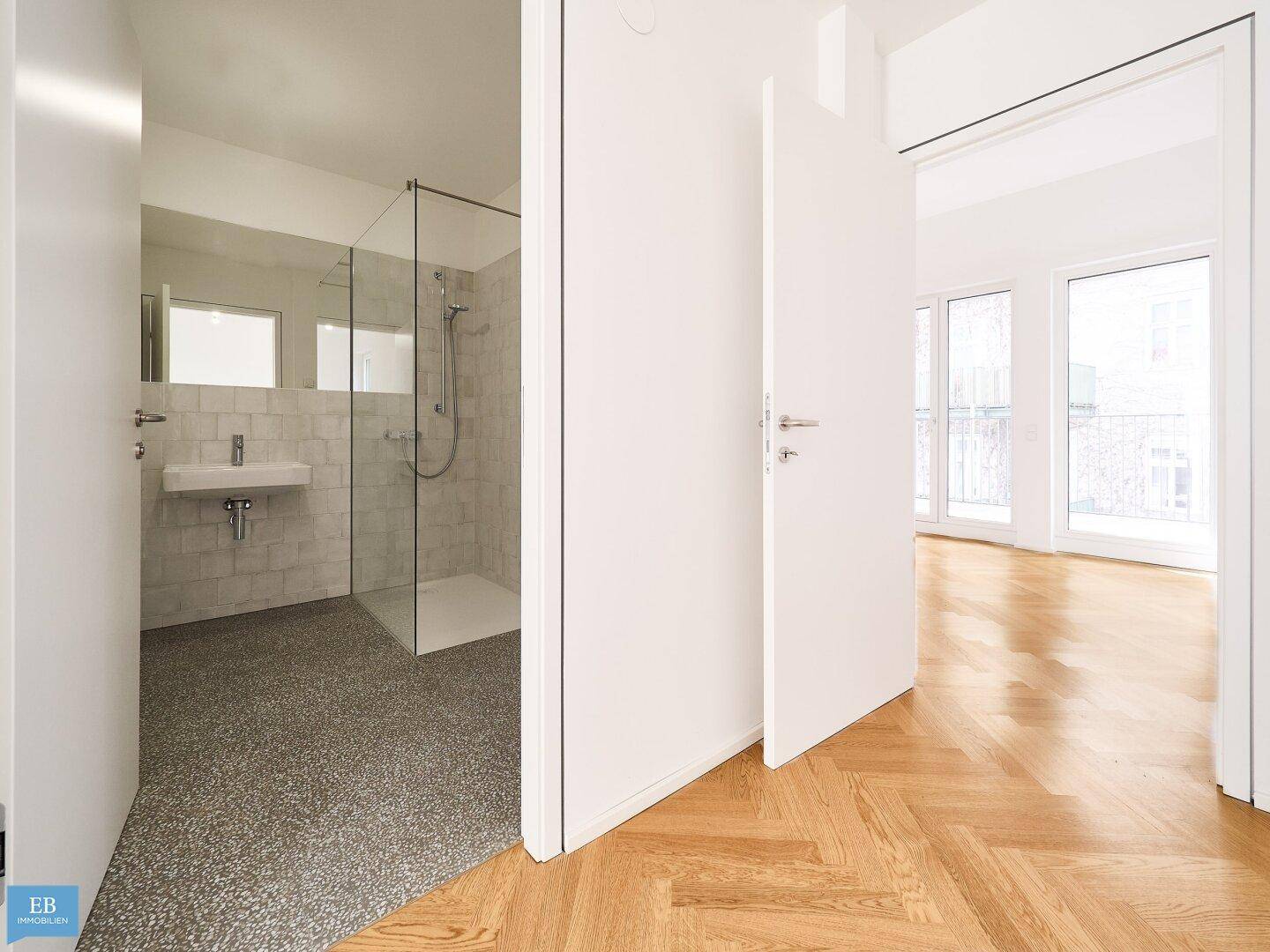 Heller Flur mit Fischgrätparkett, der zu einem modernen Badezimmer und weiteren Räumen führt.