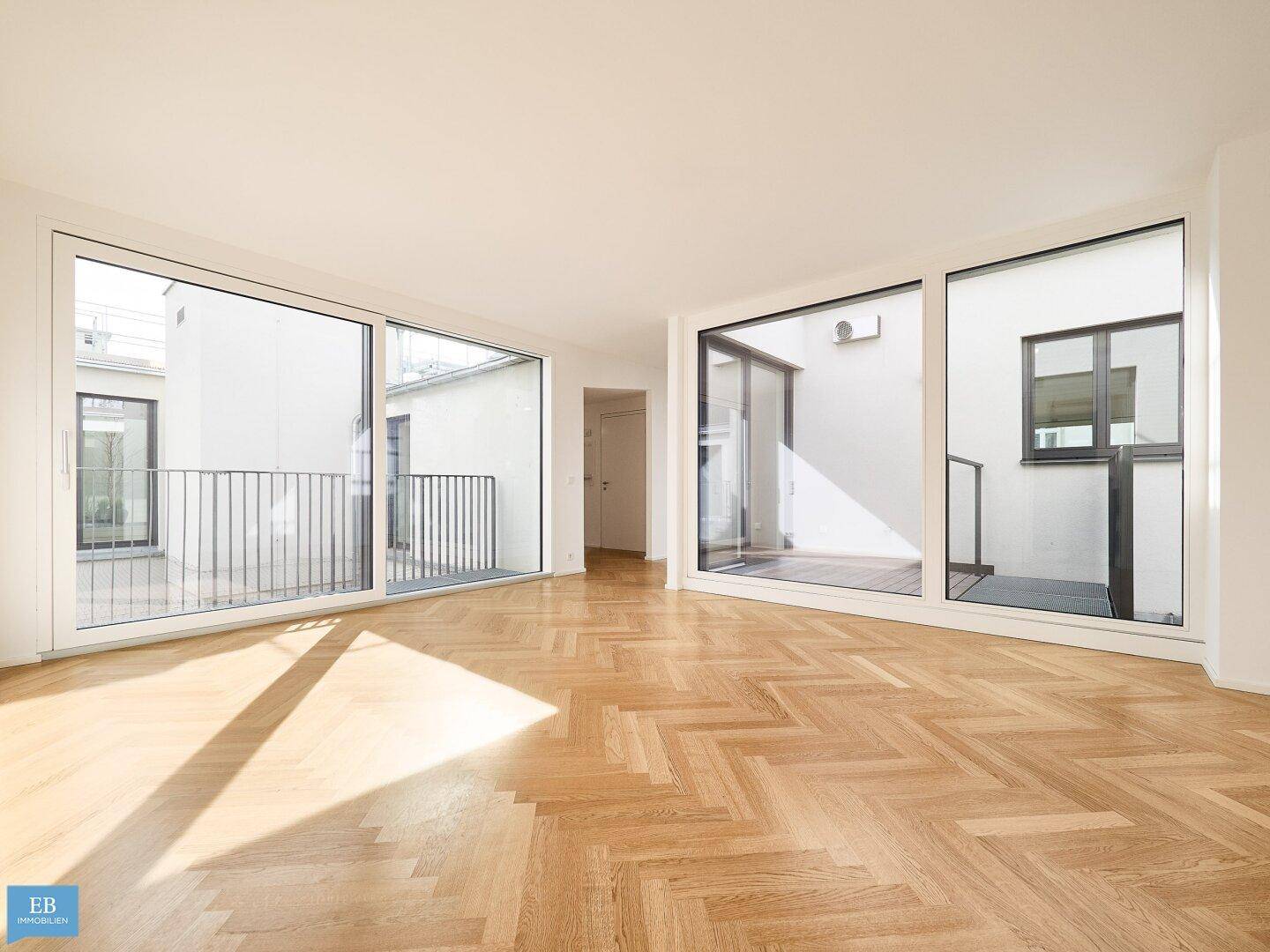 Lichtdurchfluteter Wohnraum mit Fischgrätparkett und großen Fensterfronten, die den Außenbereich integrieren.