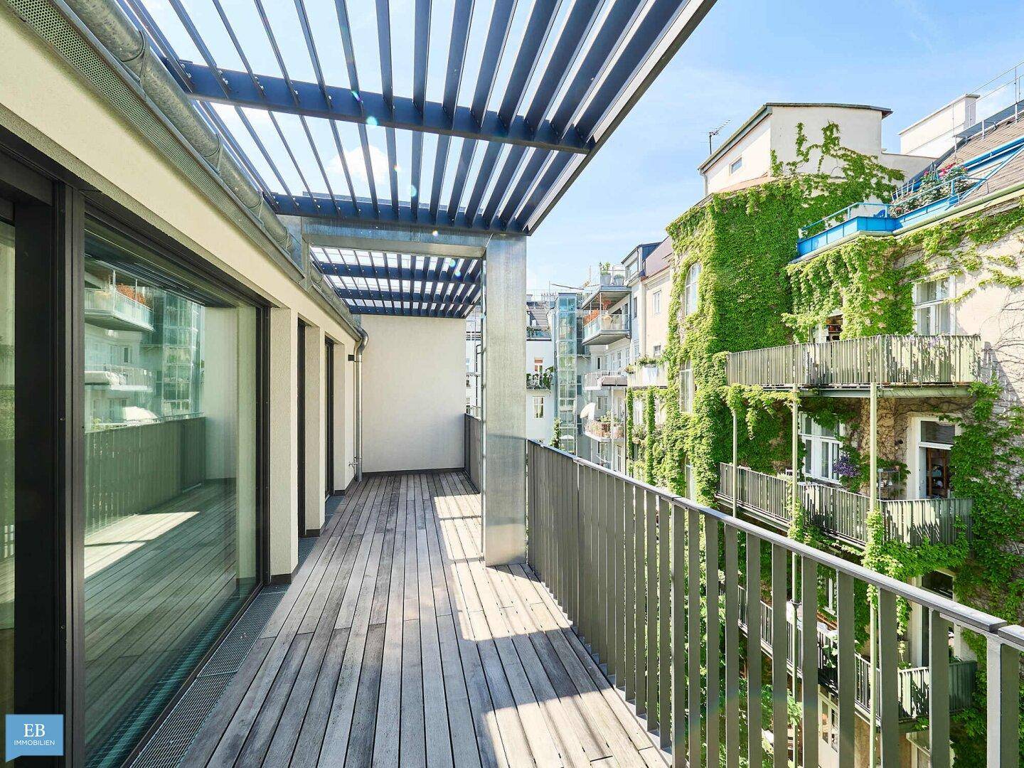 Moderne Holzterrasse mit Pergola und Blick auf begrünte Fassaden und umliegende Gebäude.